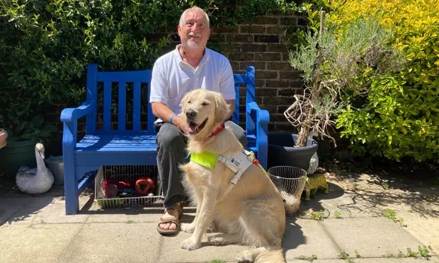 Photograph of service user Dave Kent sitting on a bench with guide dog Faldo sat on the floor in front of Dave. 