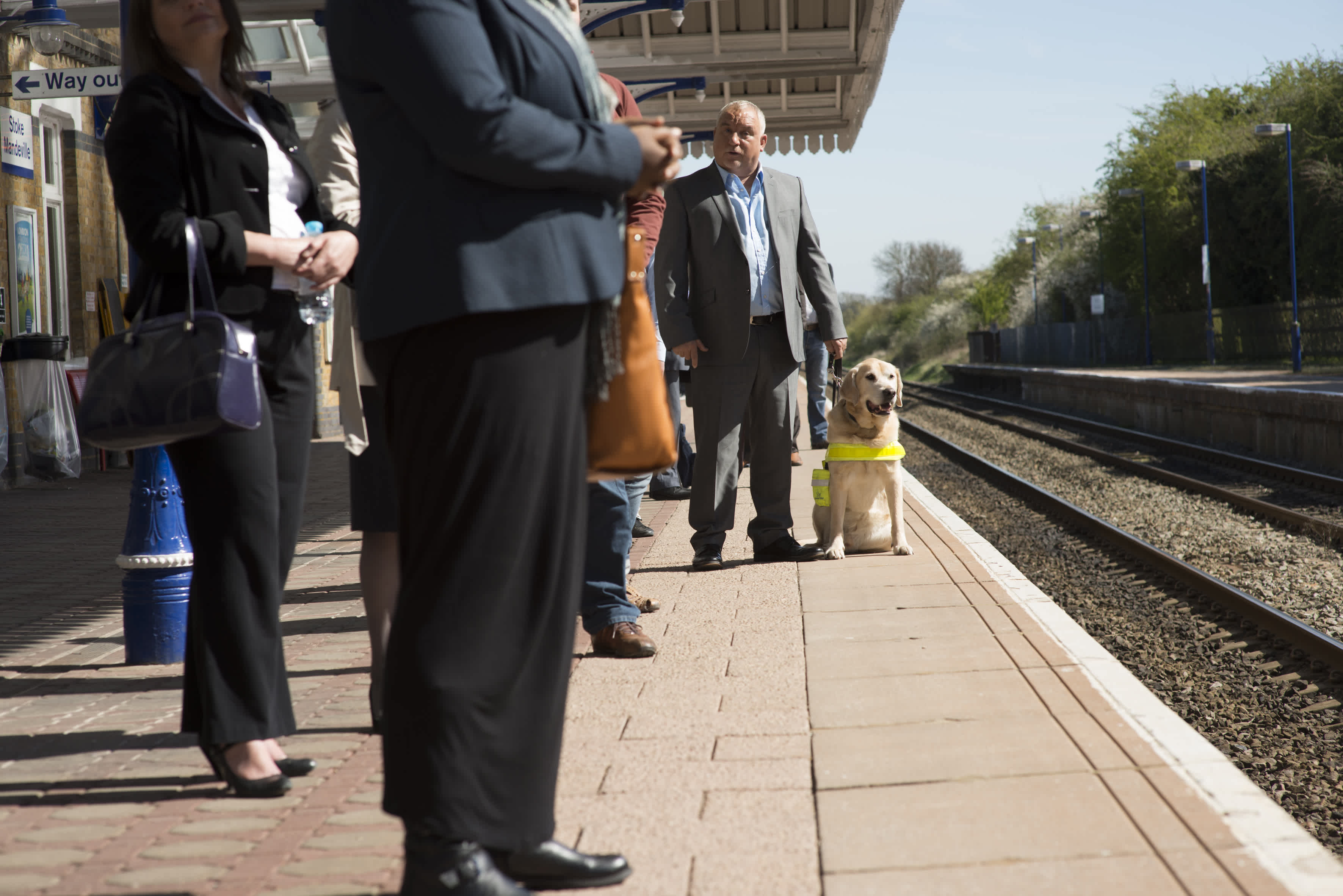 Male guide dog owner standing with his guide dog on a train platform. 