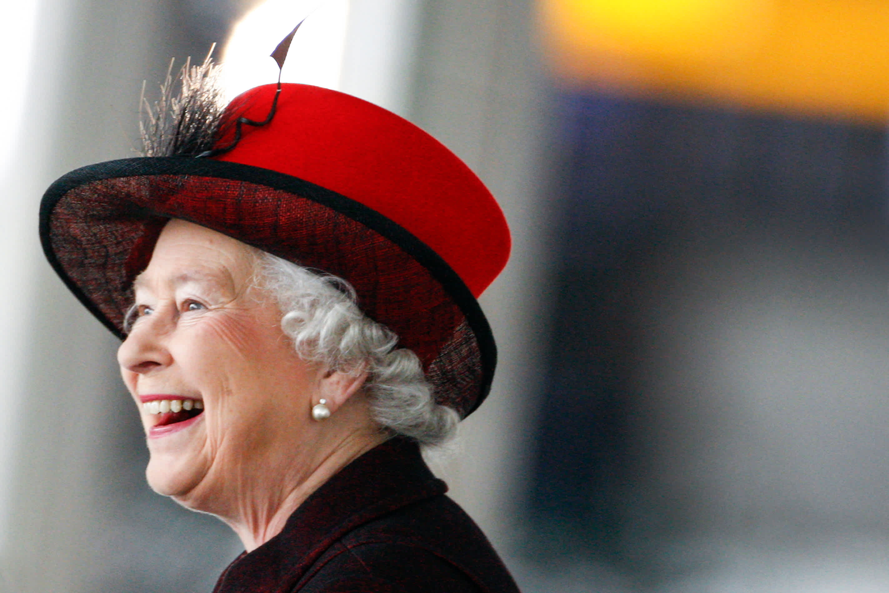 Close-up portrait of Her Majesty The Queen smiling at something out of frame and looking very happy. 