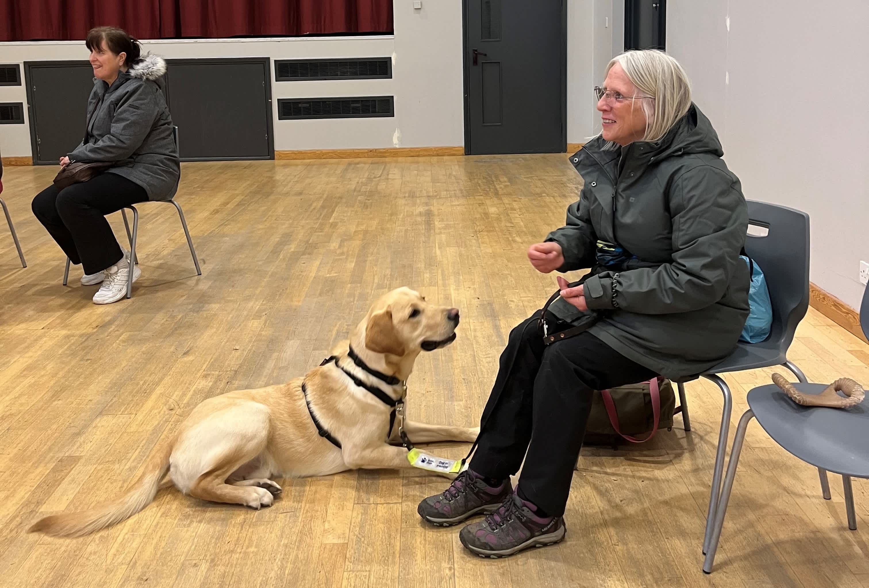 Roz sitting on a black chair with yellow Labrador retriever Nardo sat at her feet looking up at her.