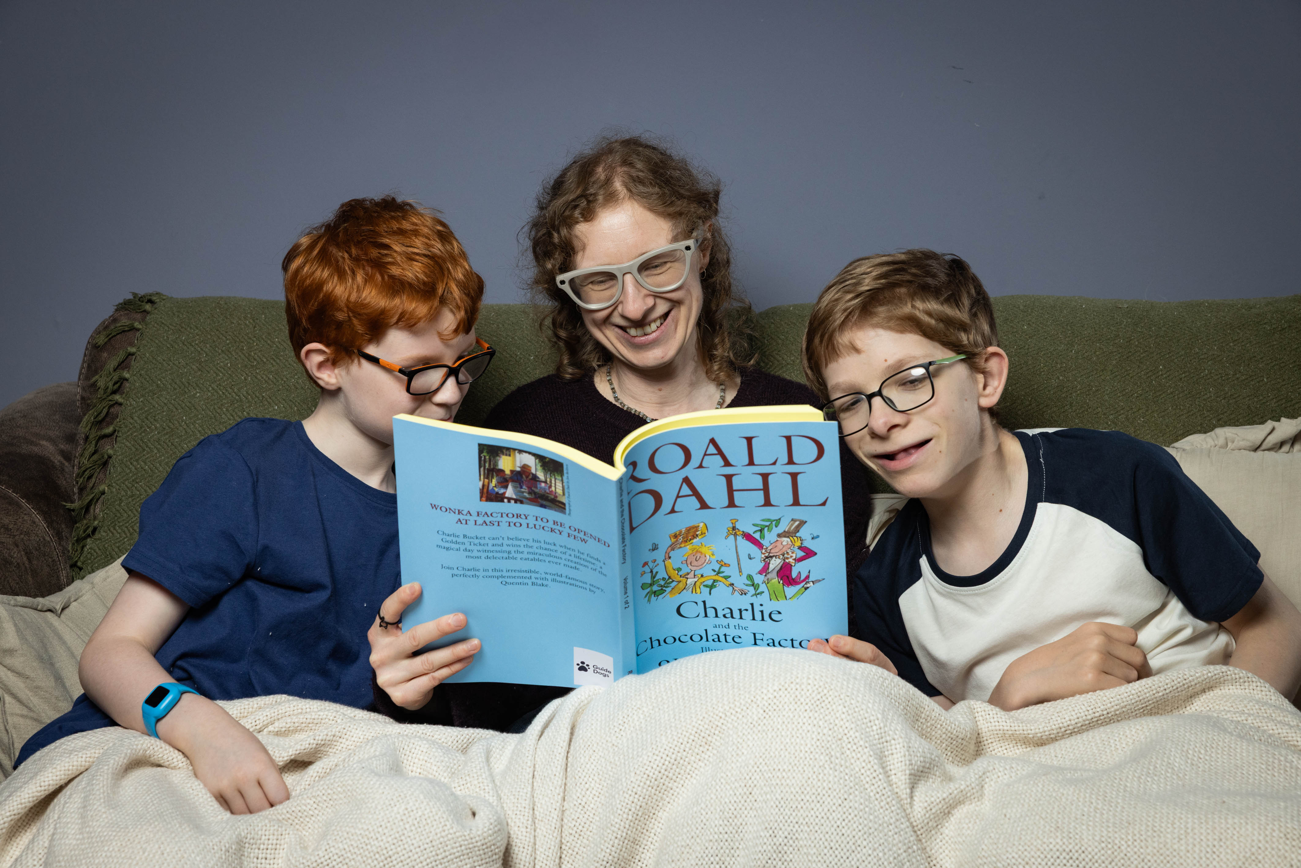 Mum Becky sits on the sofa under a blanket inbetween her two sons (aged 9 and 12). They are reading a large-print version of Roald Dahl's 'Charlie and the Chocolate Factory'. 