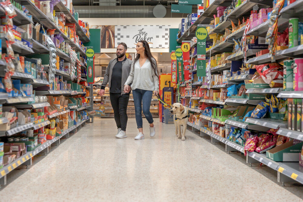 Volunteer puppy raisers Kirsty and Phil walk down a supermarket aisle with their puppy