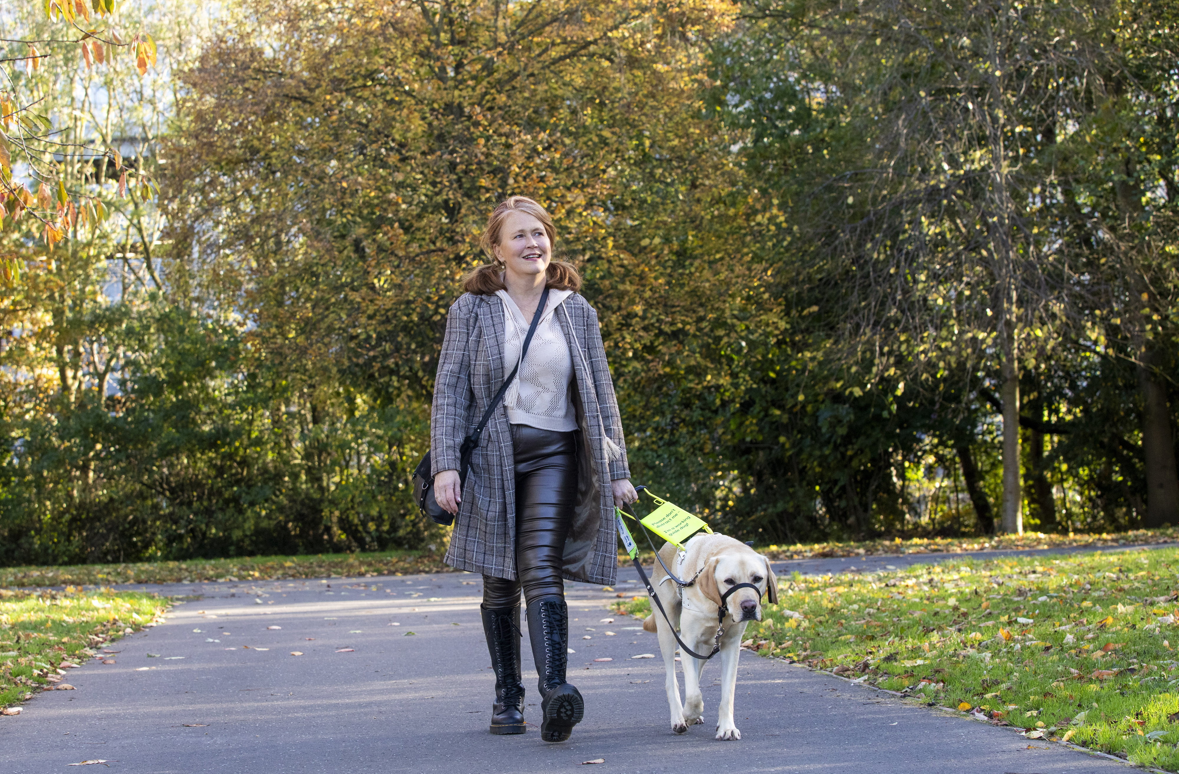 Action shot of Heather walking with guide dog Connor in harness through woodland
