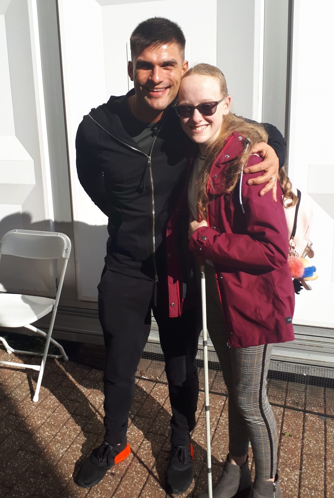 Neve stands next to Strictly star Aljaž Škorjanec. He has his arm around her while Neve holds her white cane as they both smile towards the camera. 