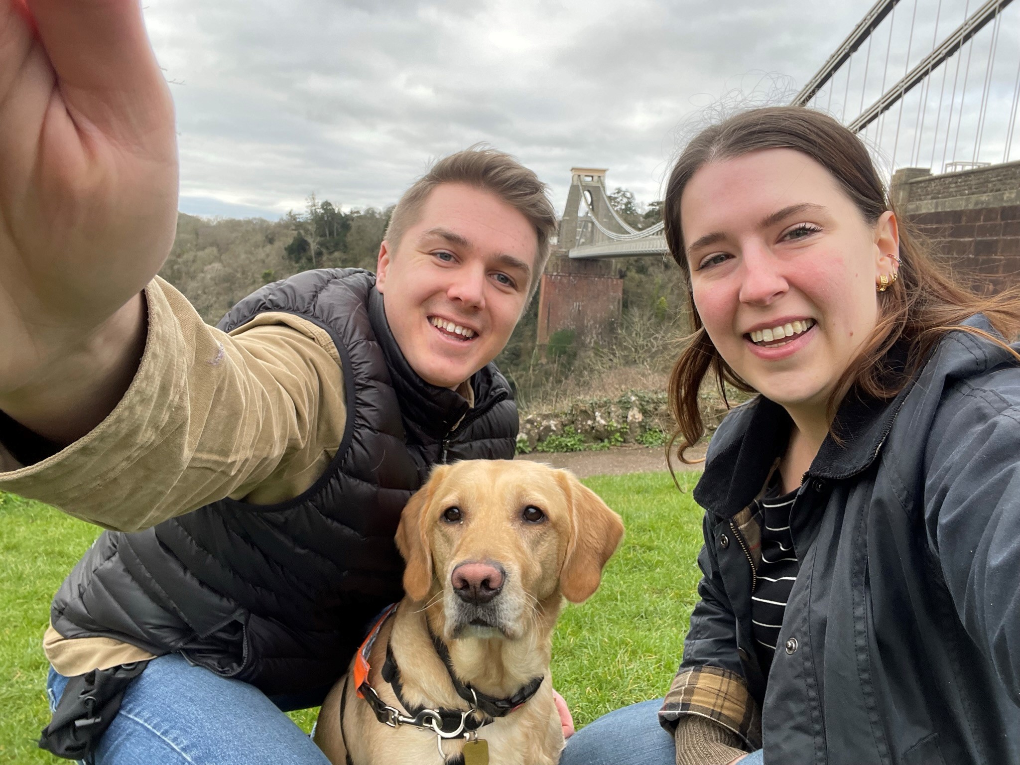 Fosterers Adam and Elle take a selfie outside with a yellow Labrador guide dog in training 