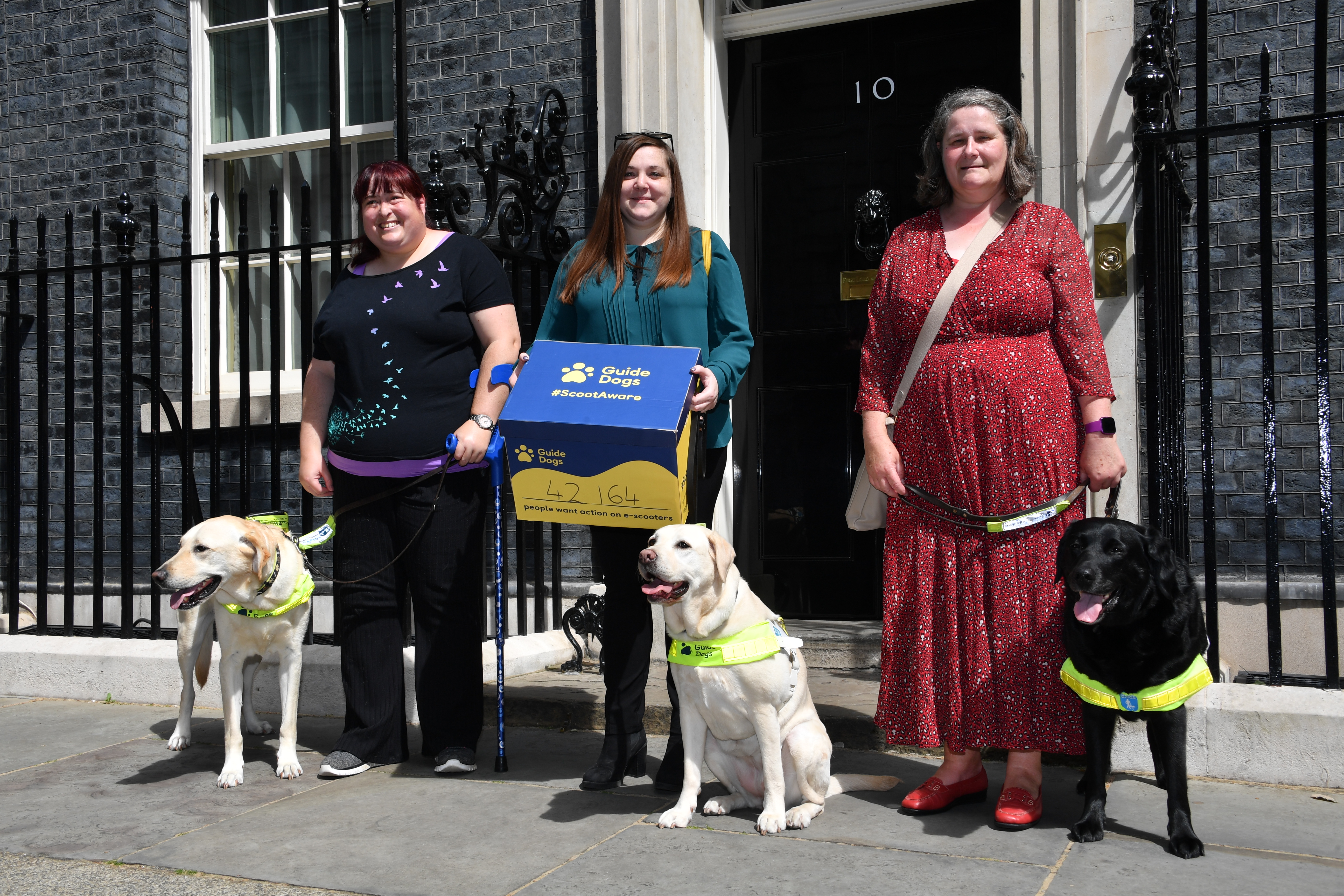 Guide dog owners Laura Drew, Sam Leftwich and Elaine Maries outside No10 with the Guide Dogs e-scooter petition, photographed with guide dogs Jimmy, Lizzie and Inca.