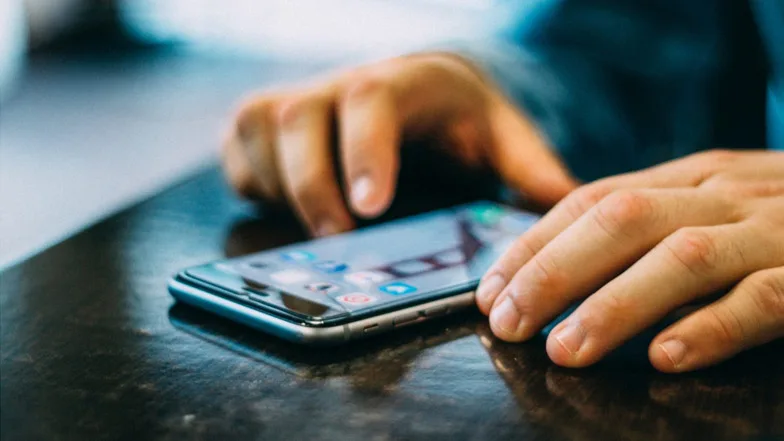 A smartphone lying on a table, with someone's hands either side as it about to use it.