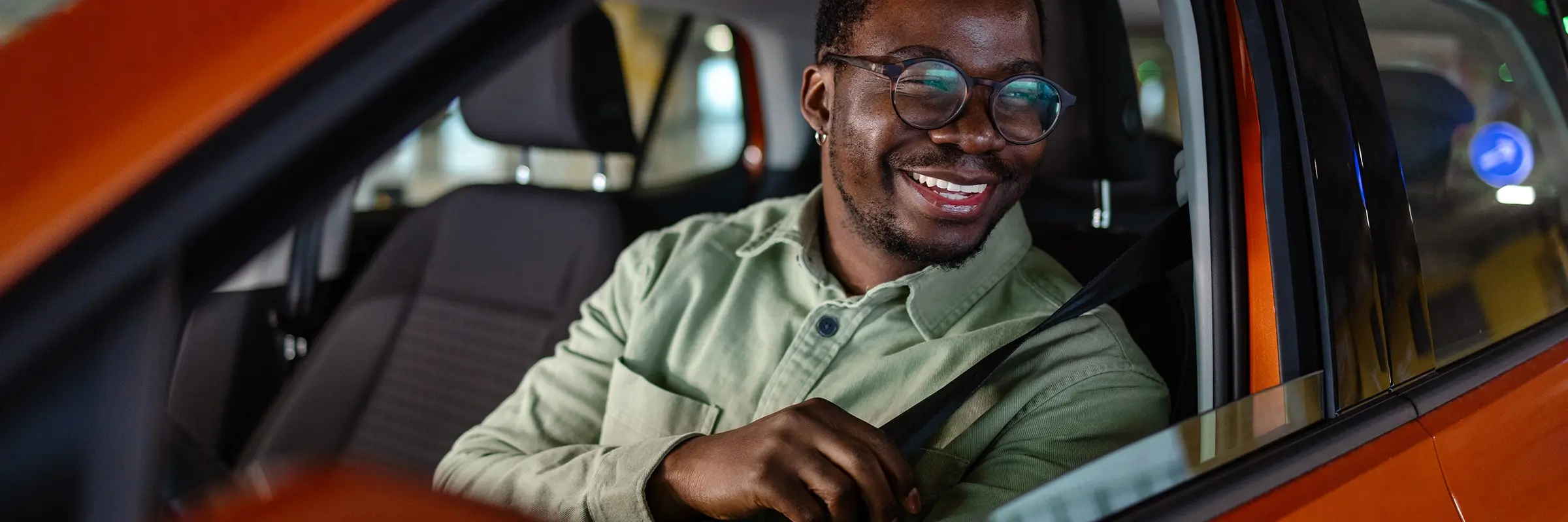 Man smiles as his sits in the drivers seat of his new car.