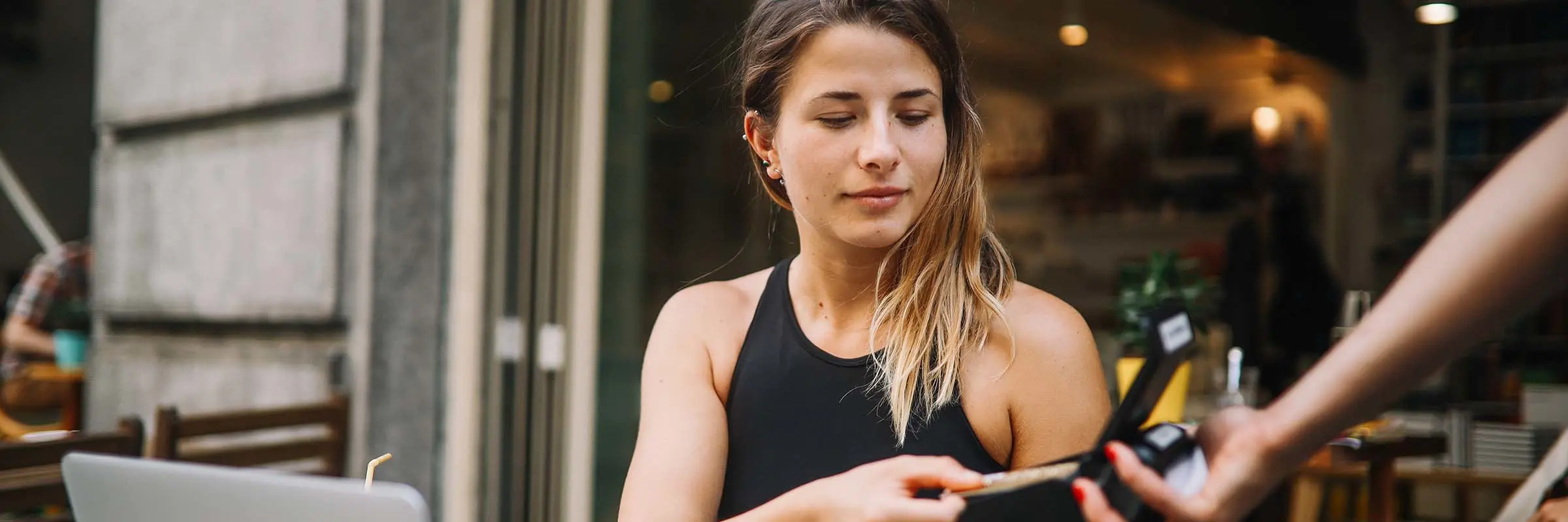 Young woman sitting at a table at a cafe pays for her coffee.