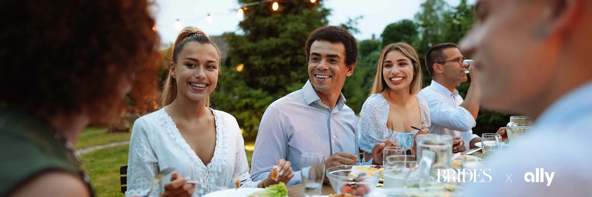 Group of young men and women enjoy an outdoor meal under string lights