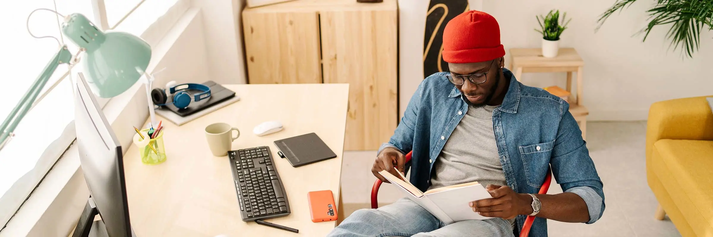 Image of a man reading a book with his feet up on his desk