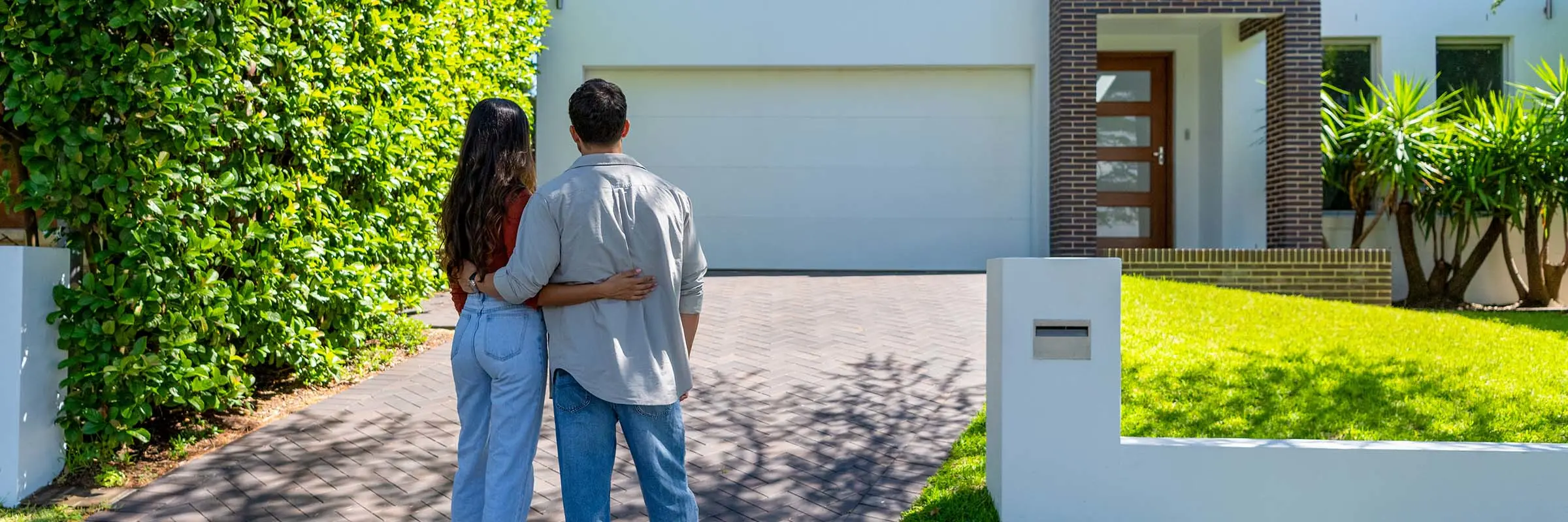 Couple stands outside of a home on a sunny day.