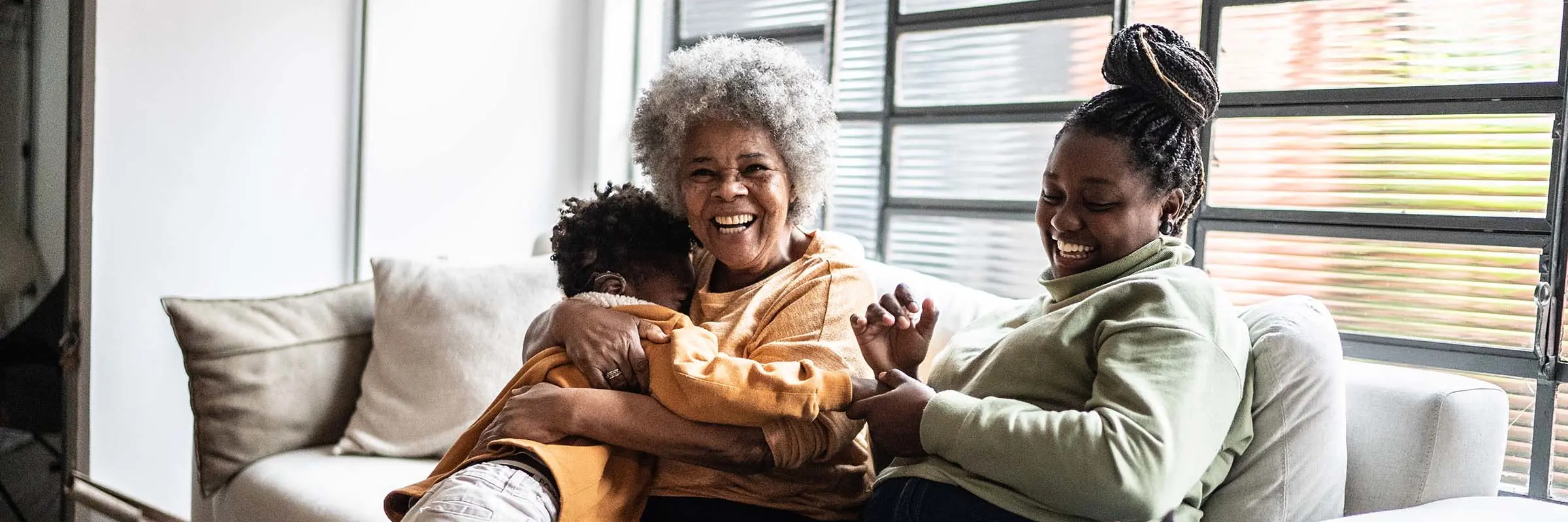 A child hugging and playing with his grandmother and mother in a living room