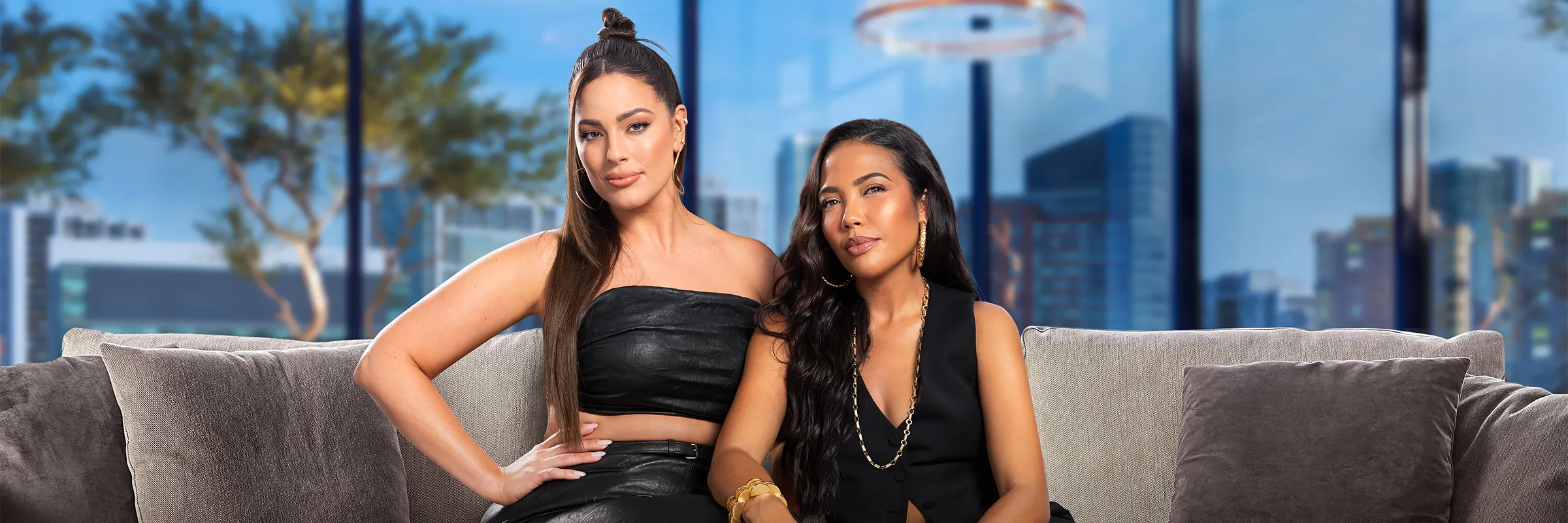 Ashely Graham and Emma Grede sit on a couch on the set of Side Hustlers television show