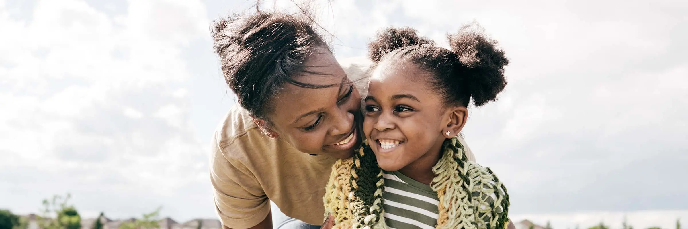 Mom hugging daughter from behind while playing outside