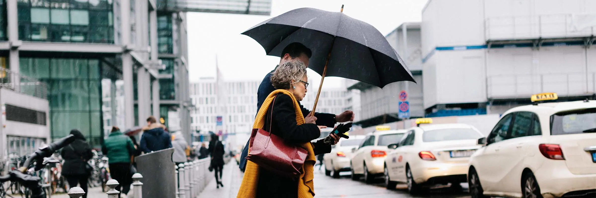 A couple crosses the street in the rain, sharing one umbrella