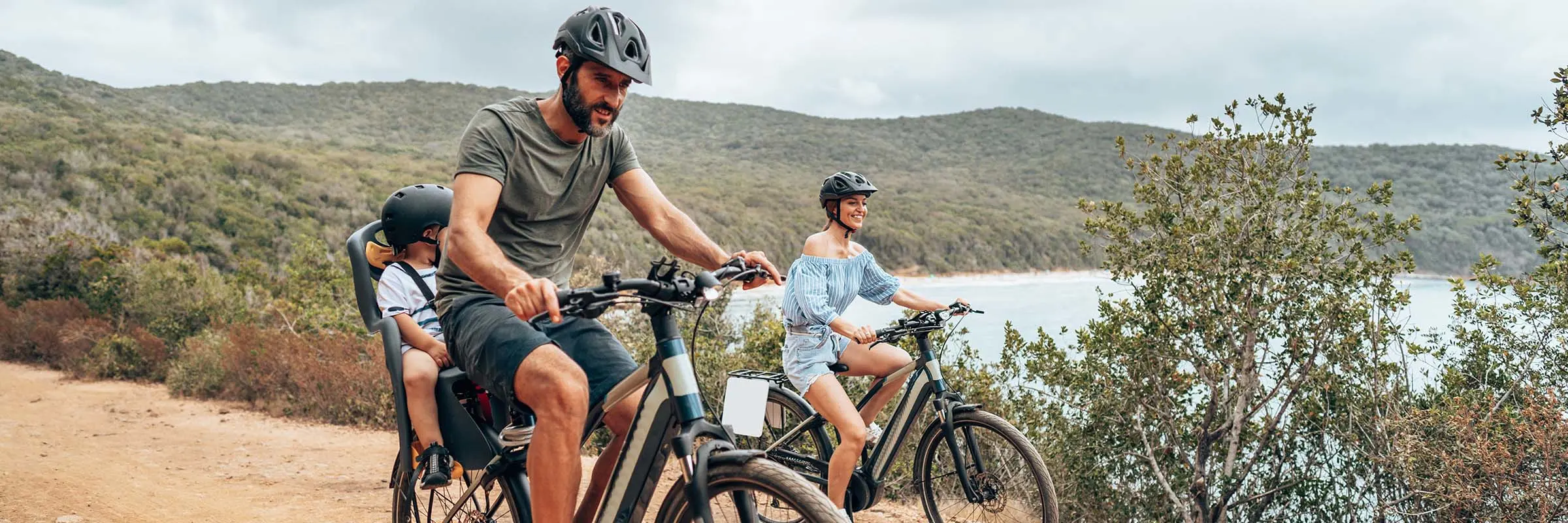 A family rides bikes on a countryside trail that overlooks a lake.