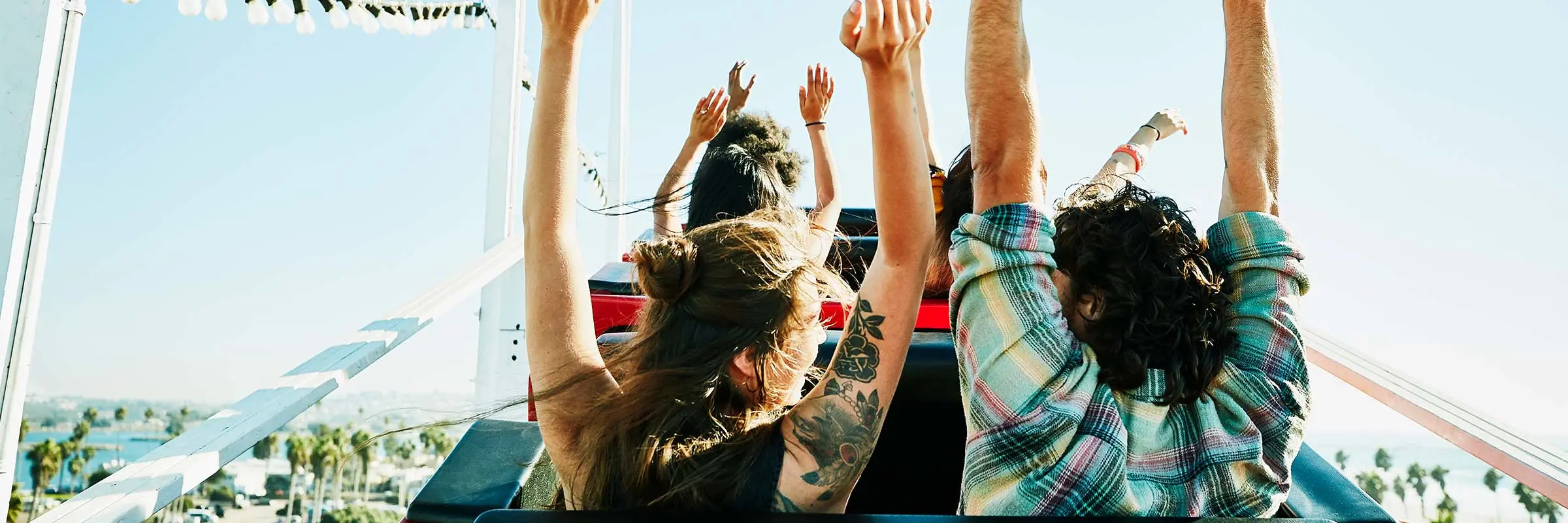 ear view of couple with arms raised on roller coaster in amusement park