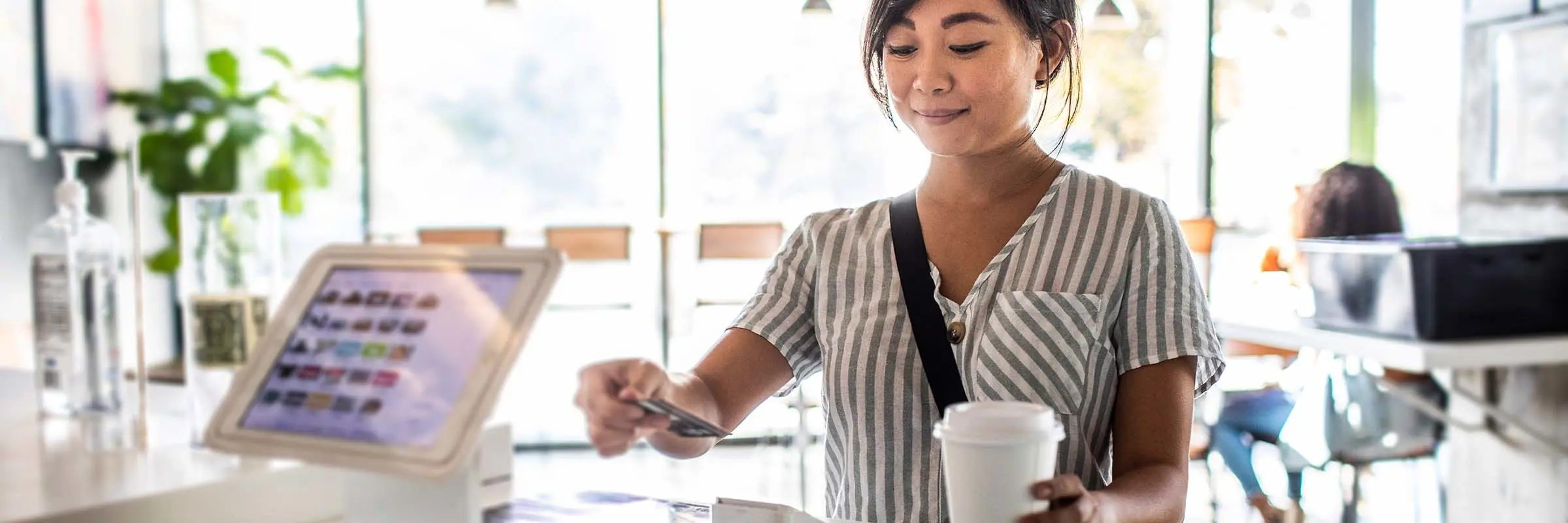 Woman uses a card reader to pay for a cup of coffee at a shop counter.