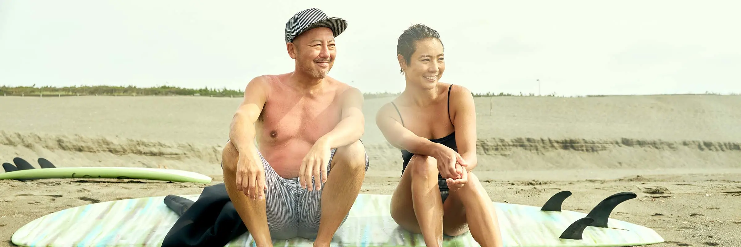 Portrait of a couple sitting on a surfboard on the beach