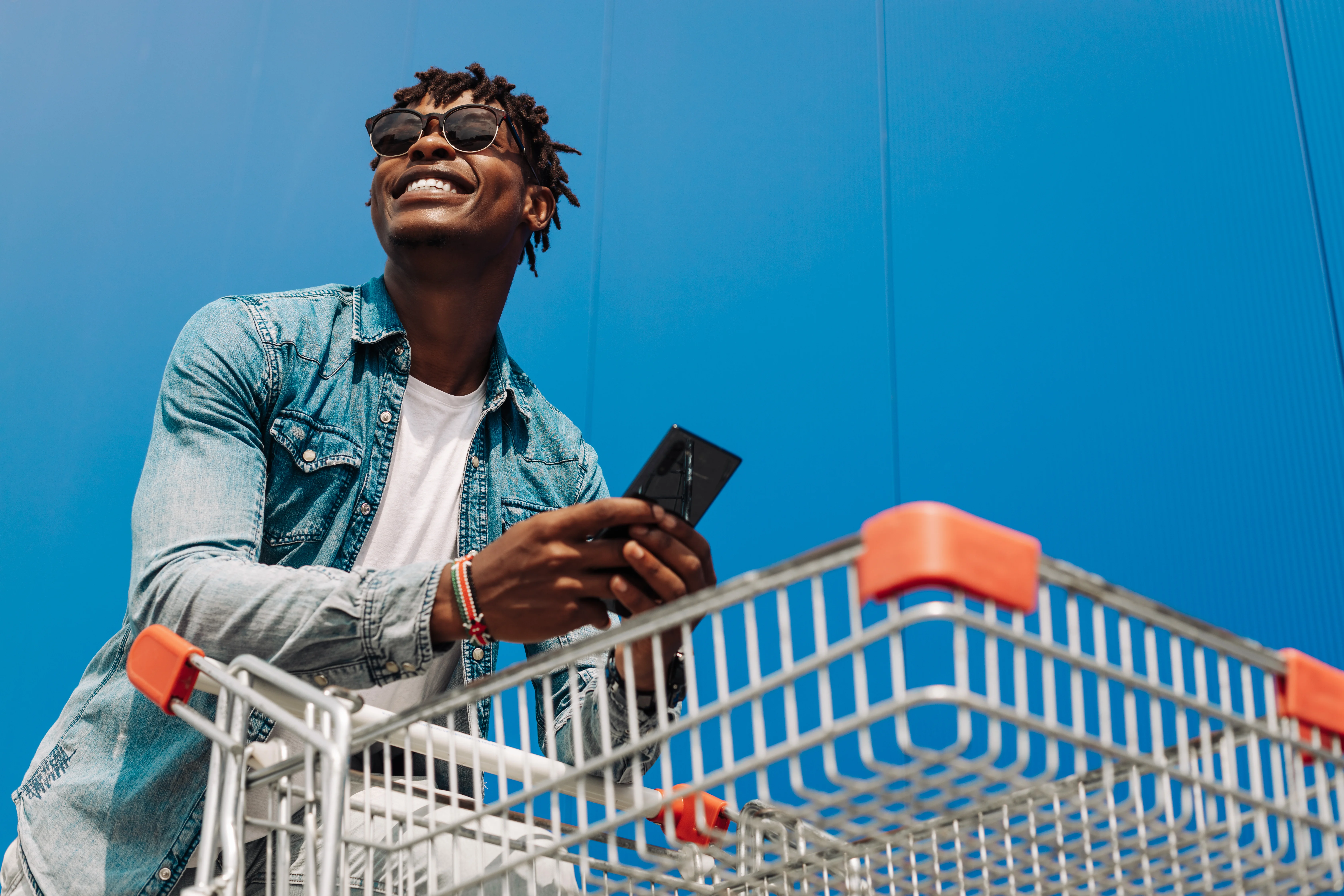 man leaning on shopping card with phone in-hand wearing sunglasses