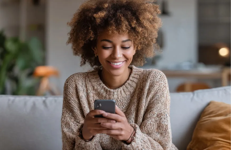 woman with curly hair sitting and smiling down at phone