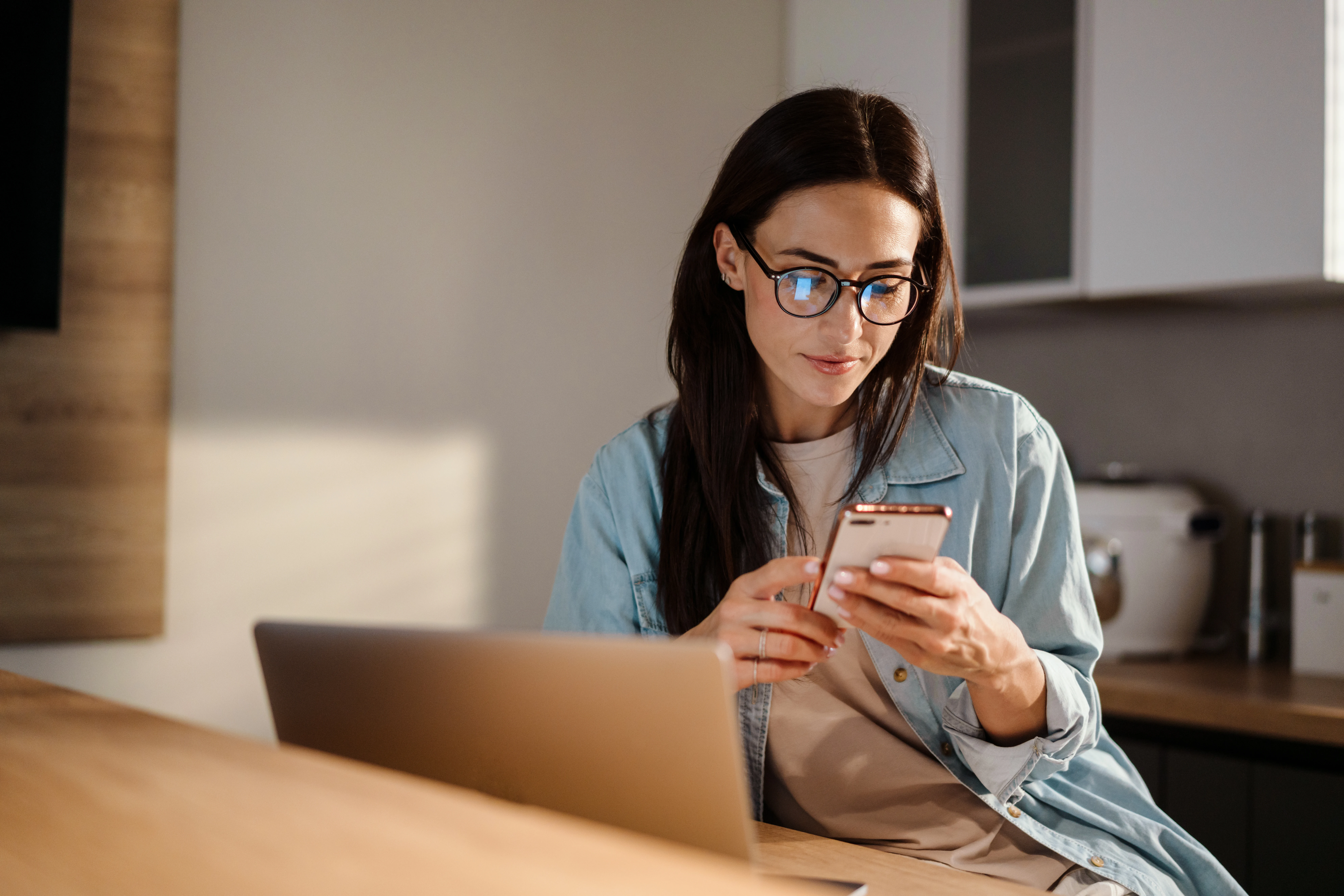 woman with glass sitting at a table and reviewing something on her phone