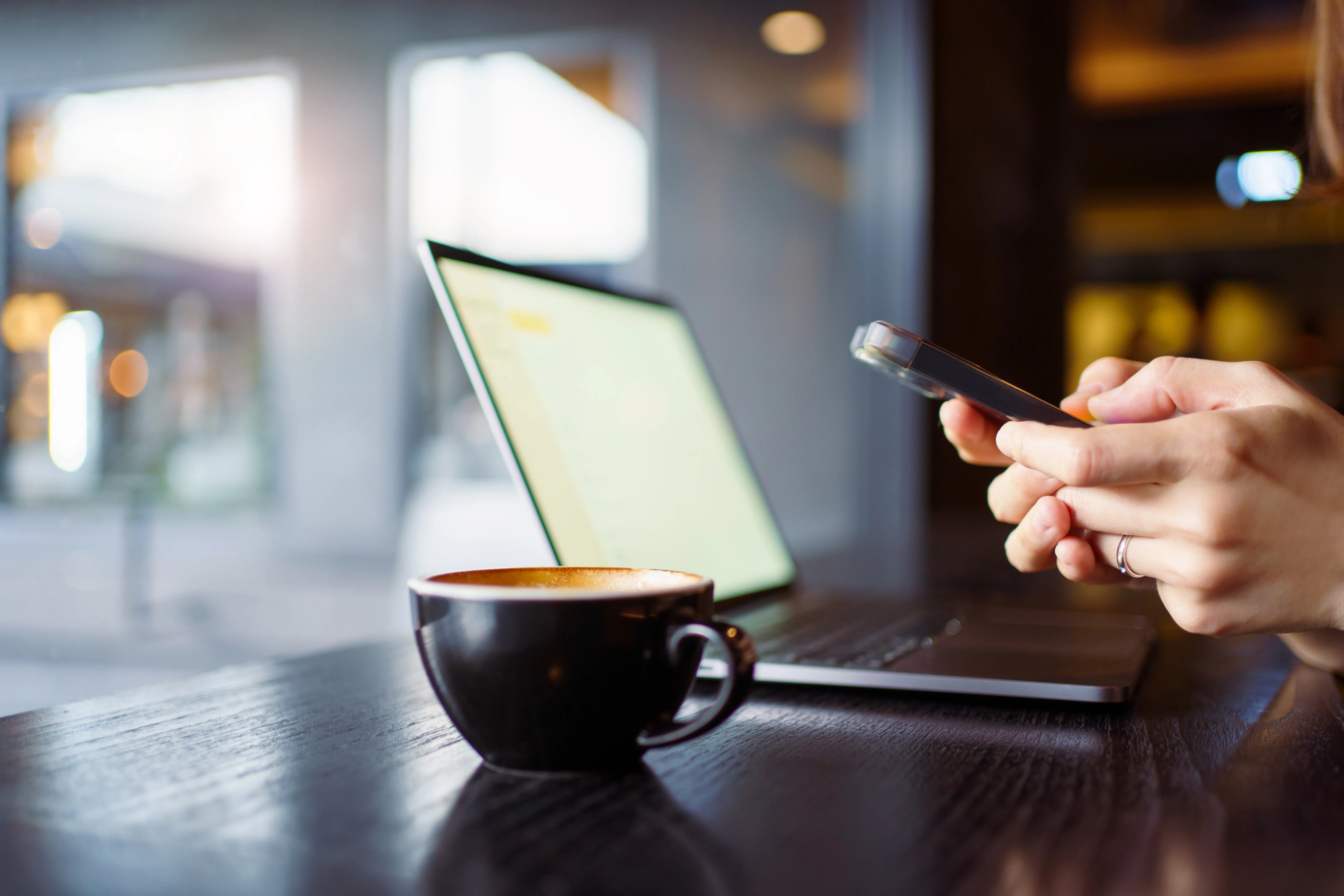 person on their phone and using computer while drinking coffee