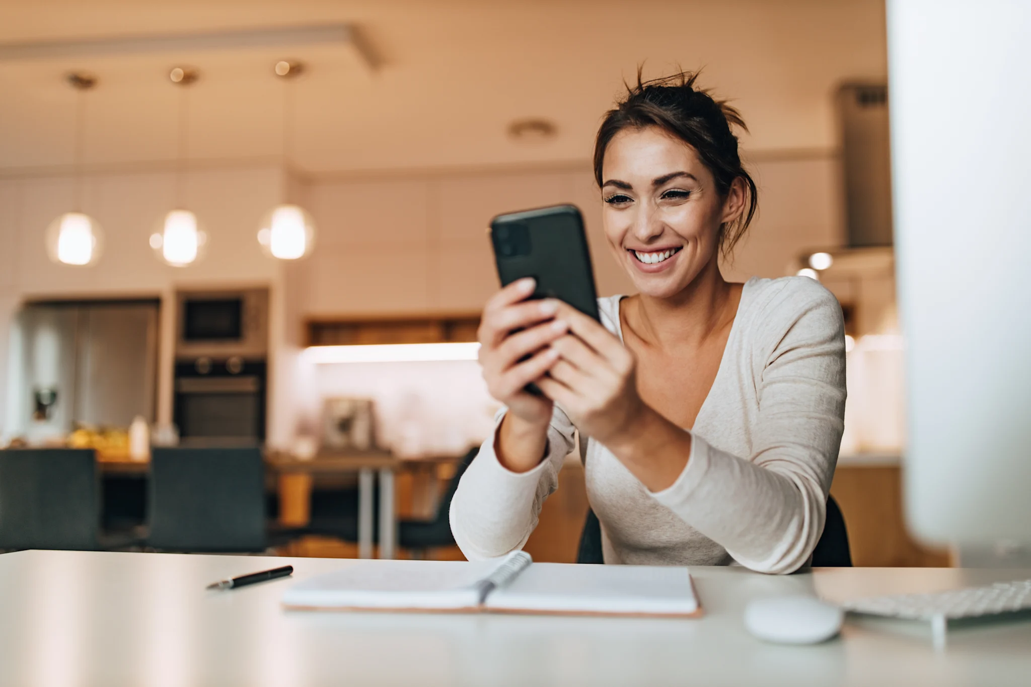 woman smiling in her kitchen while looking at her phone