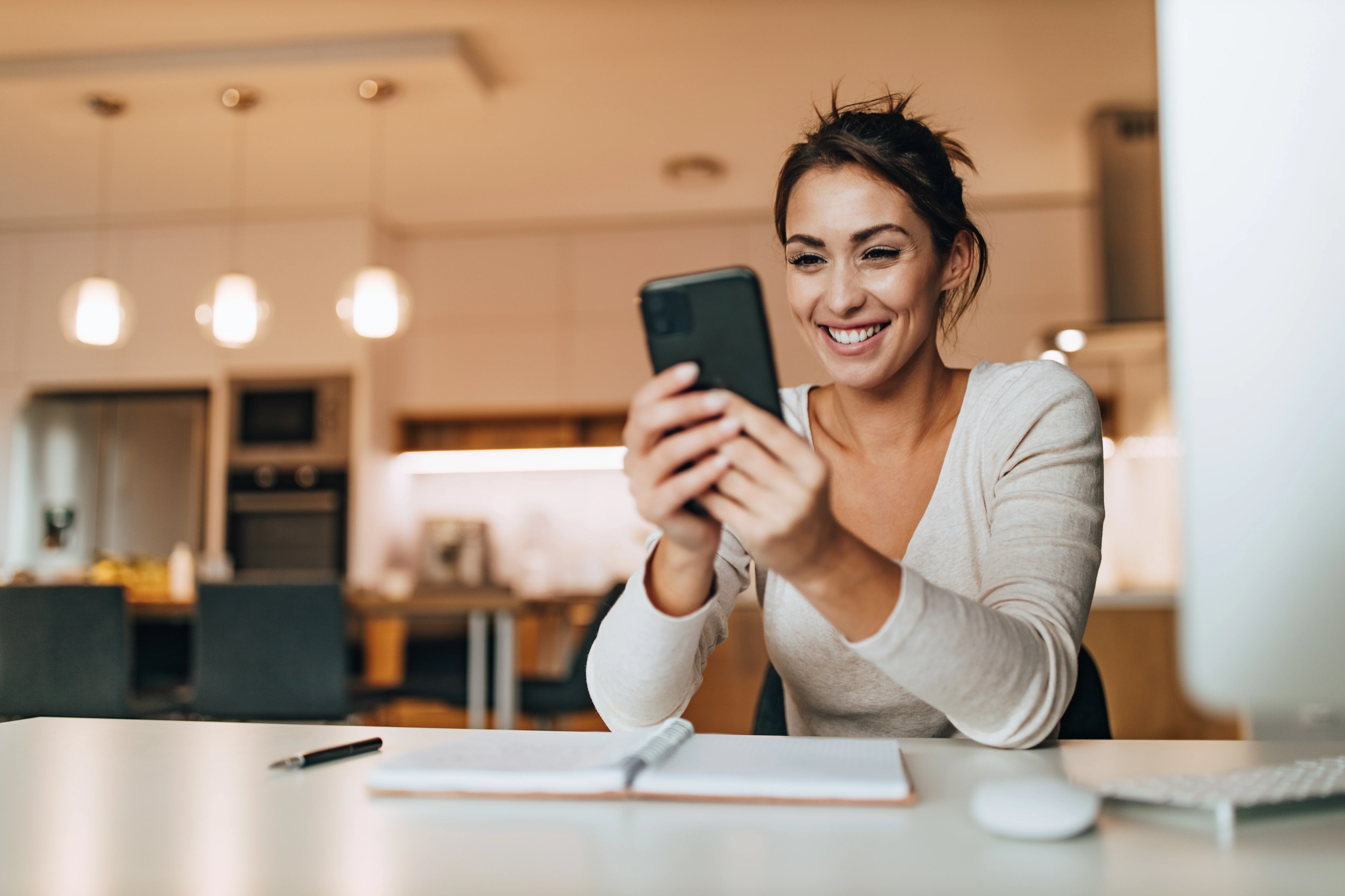 woman smiling in her kitchen while looking at her phone