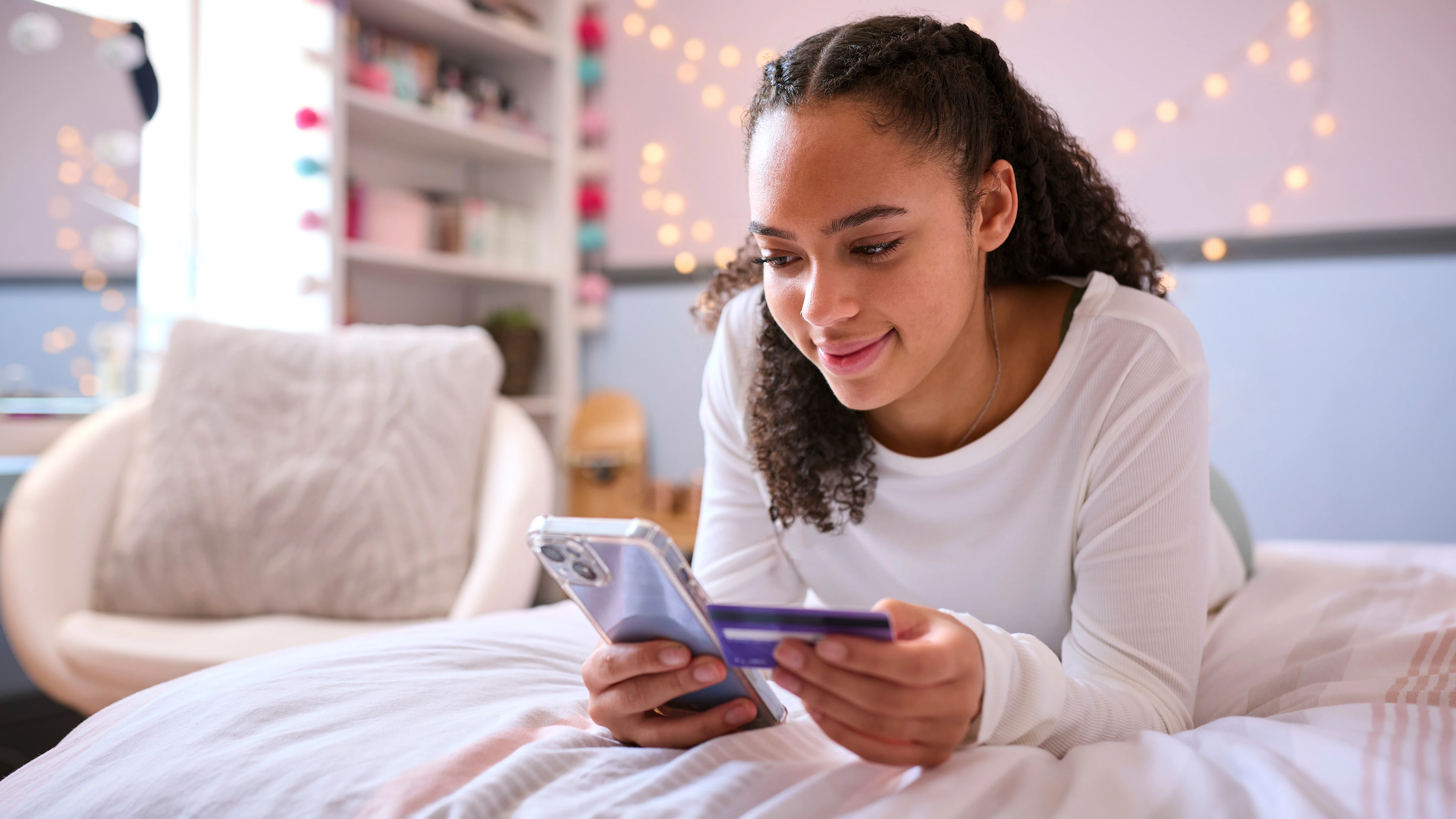 girl shopping on her phone in her bedroom with a credit card in her hand