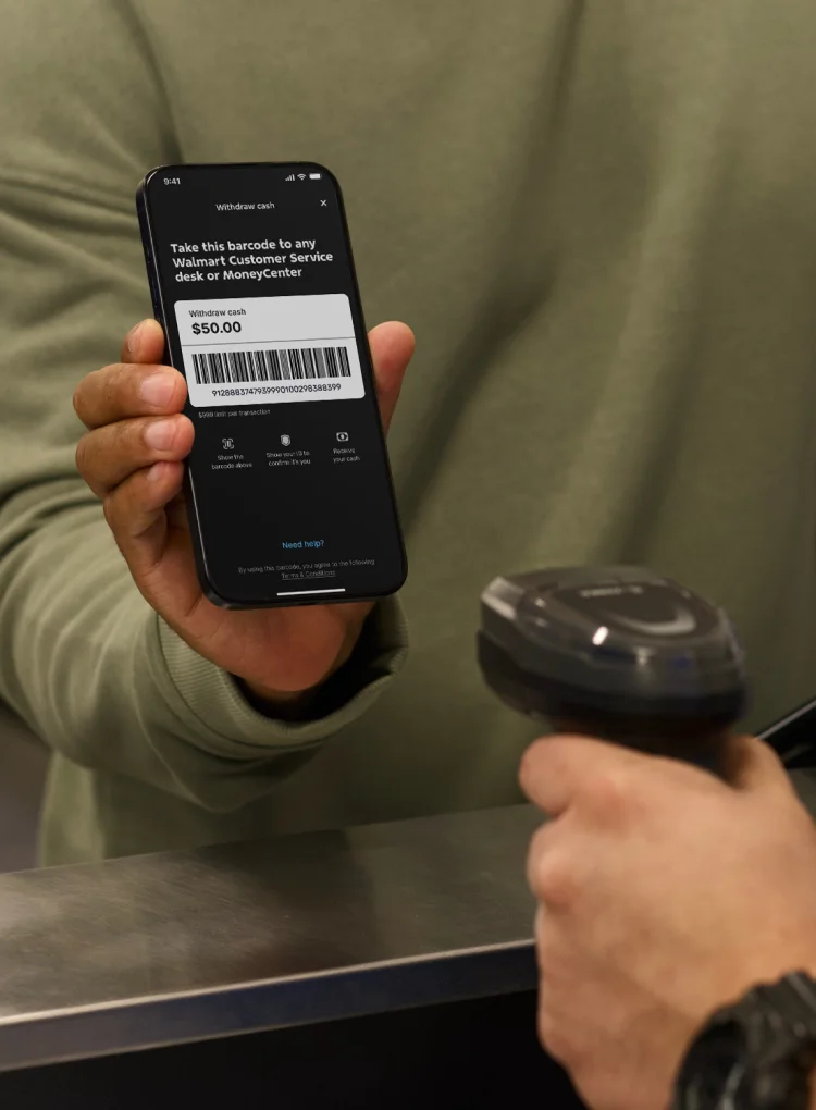 A customer holds a phone up for a Walmart associate to scan. The screen shows a barcode to withdraw cash.