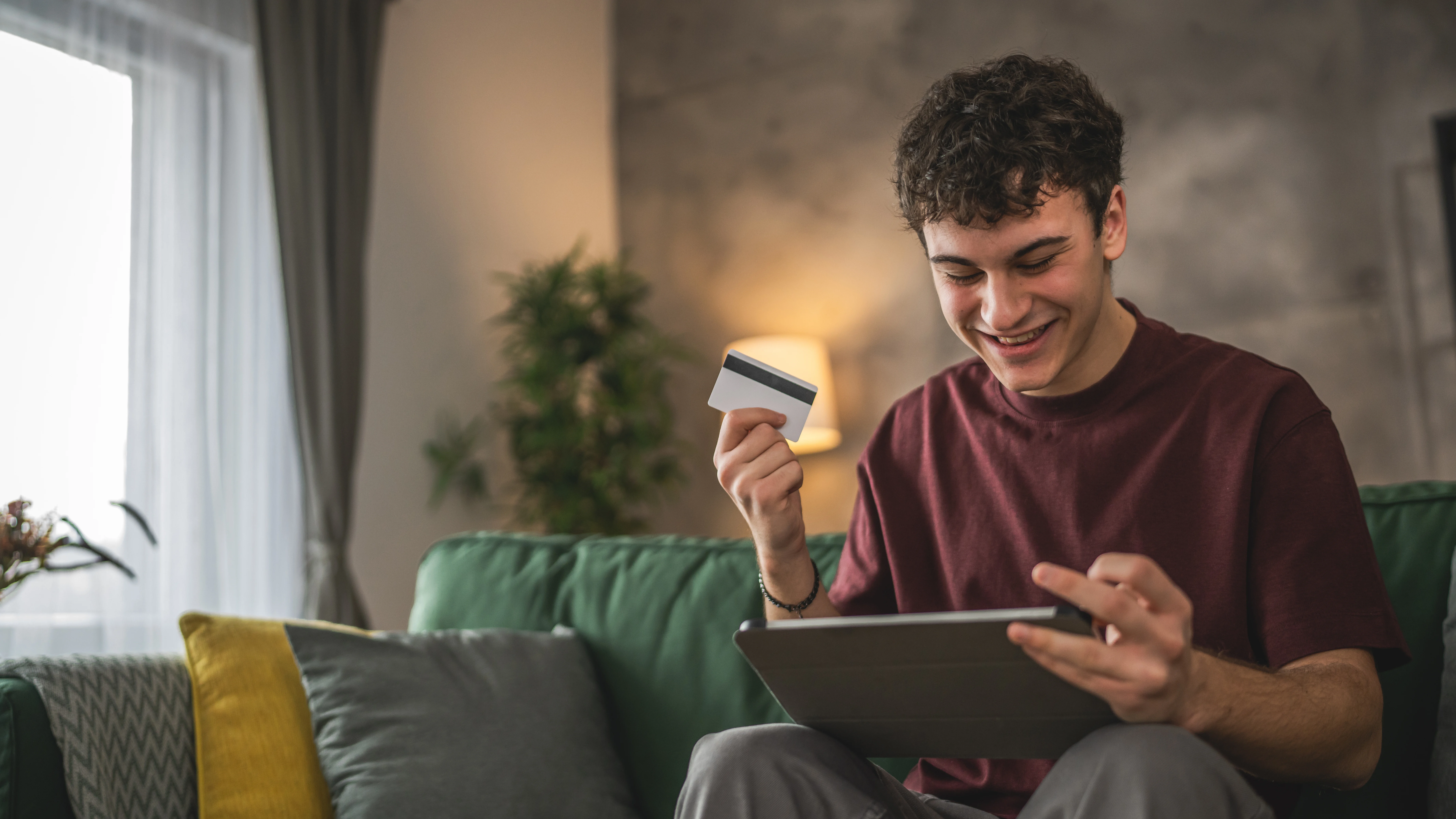 teen boy smiling while purchasing something on his phone while holding a debit card