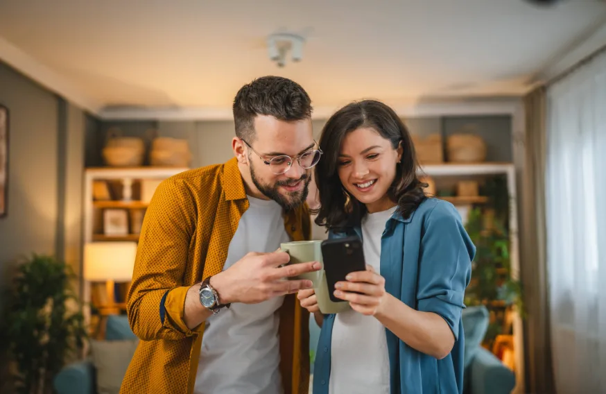 couple in living room smiling and looking at a single phone