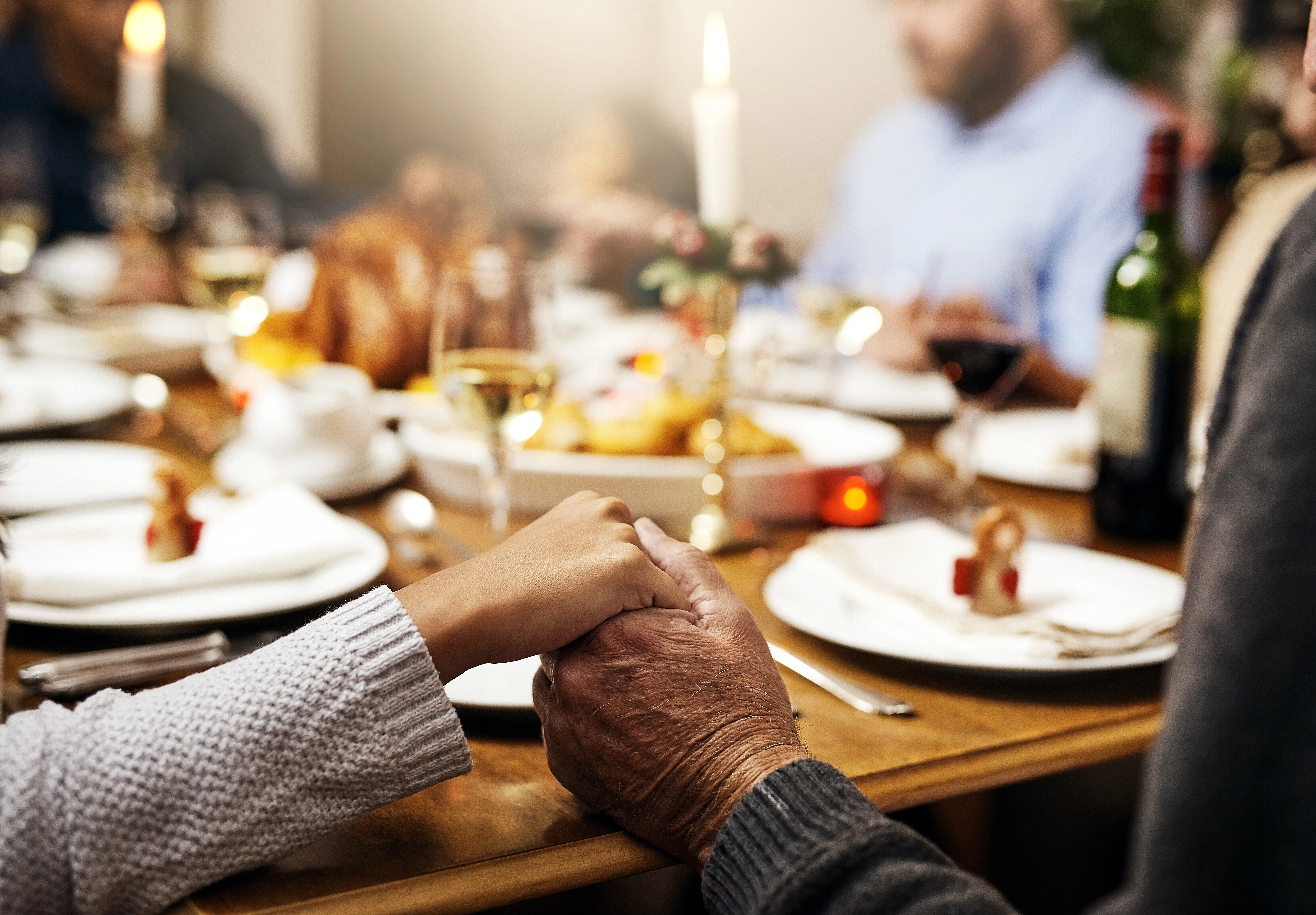 two hands holding each other at a crowded dinner table