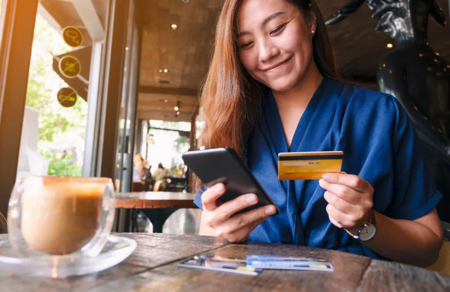 woman smiling down at phone holding a gold card