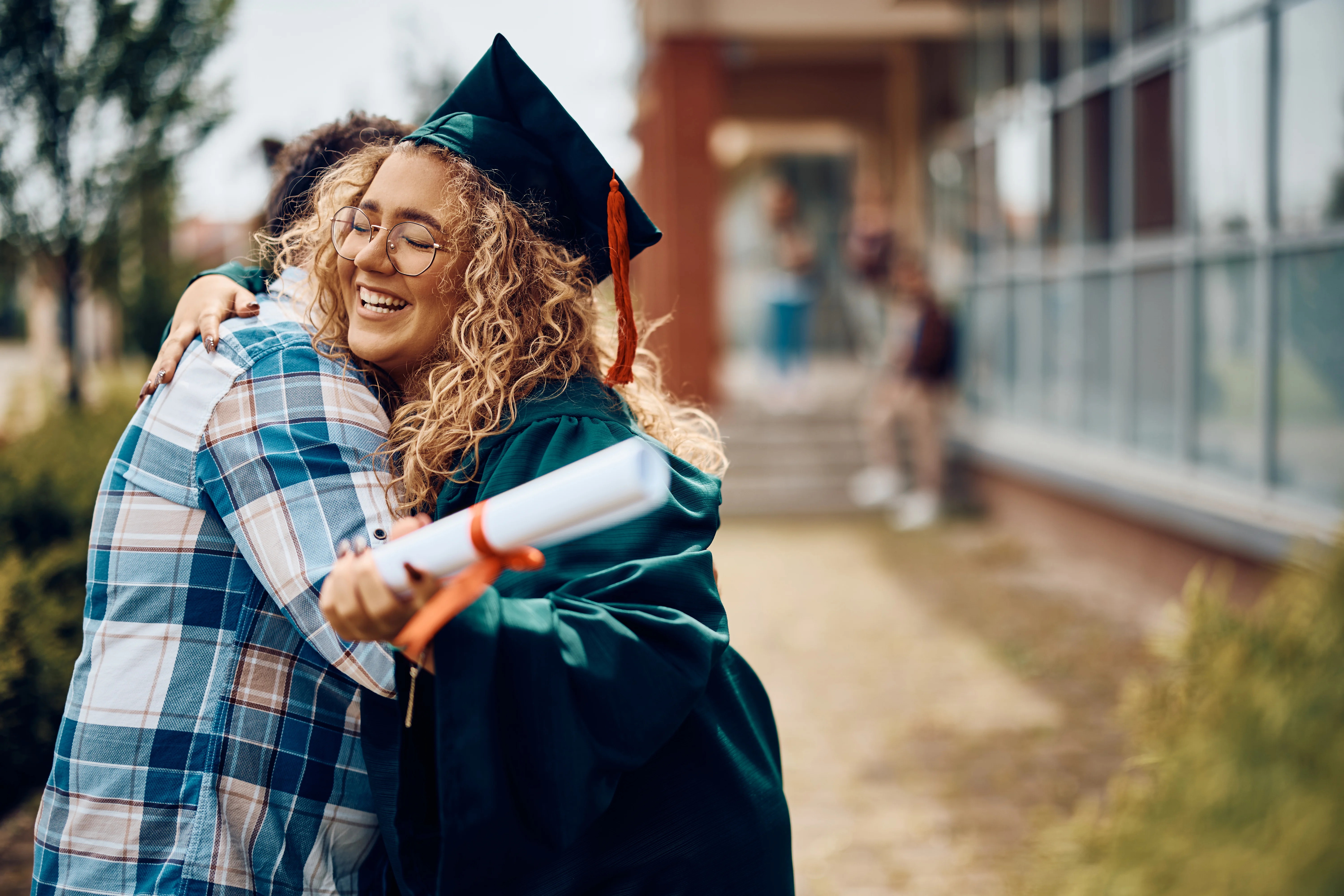 woman with long curly hair in graduation gown hugging another person