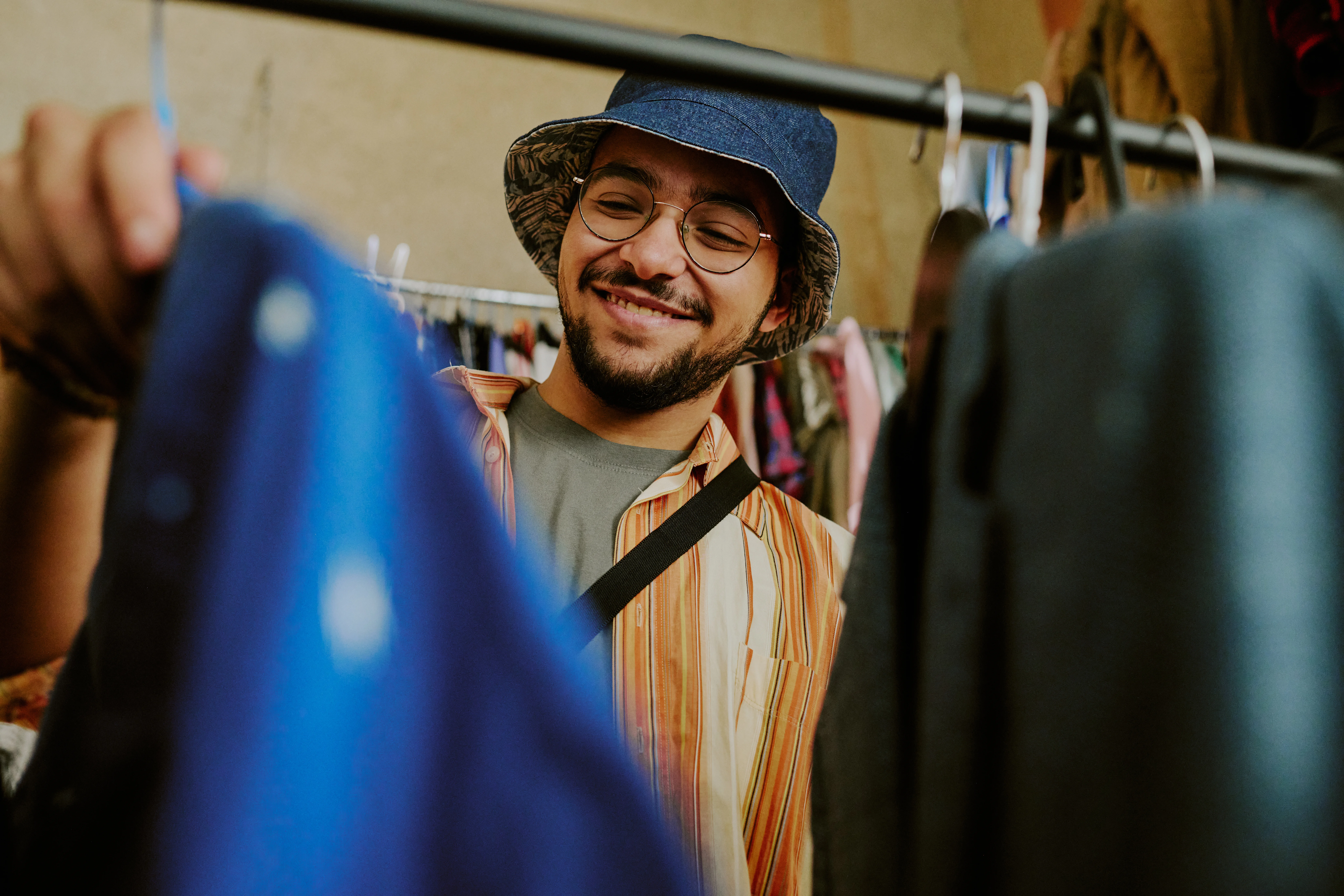 man in hat swiping through a rack of clothes