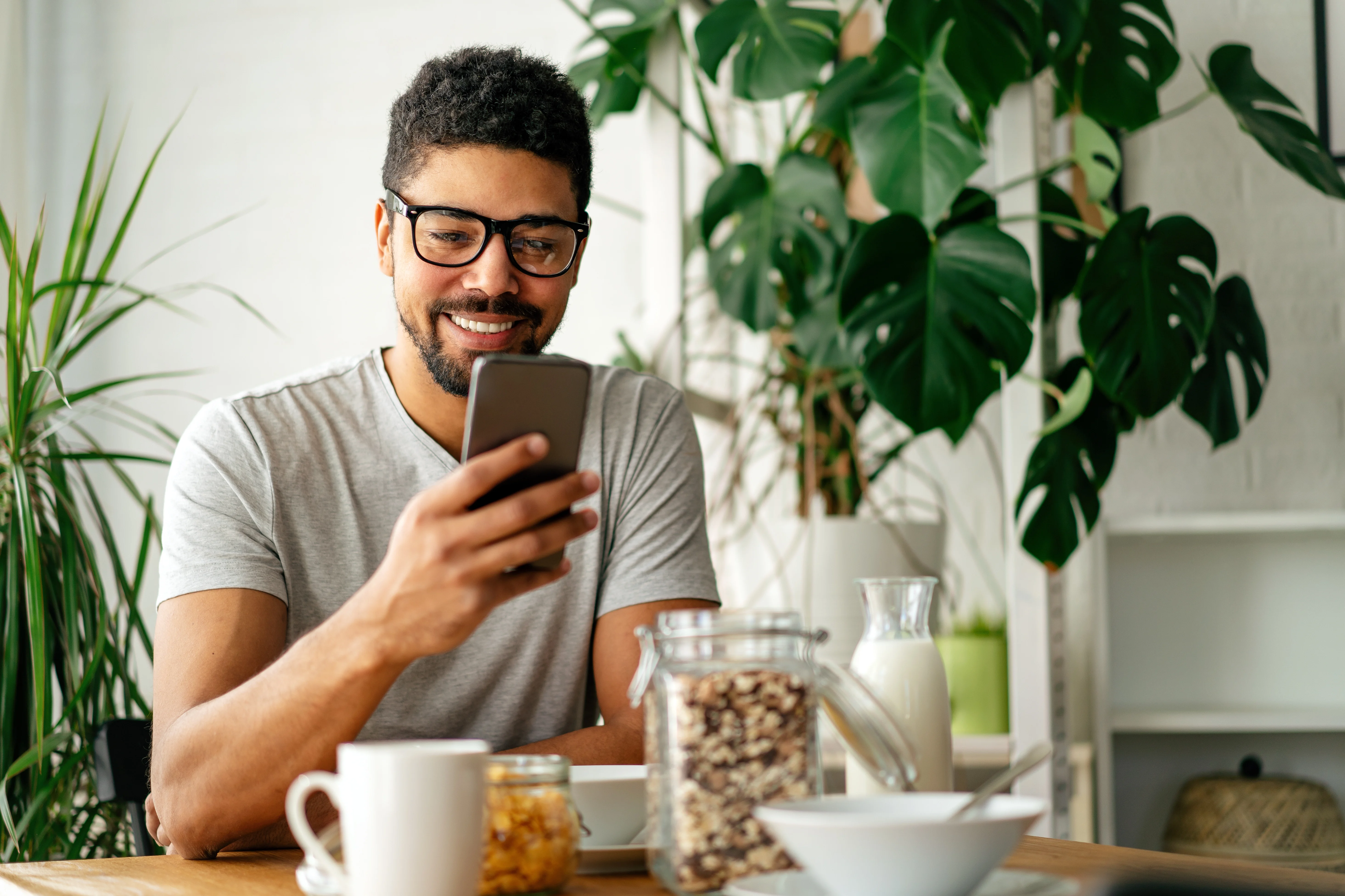 man with glasses sitting at his kitchen table scrolling through phone