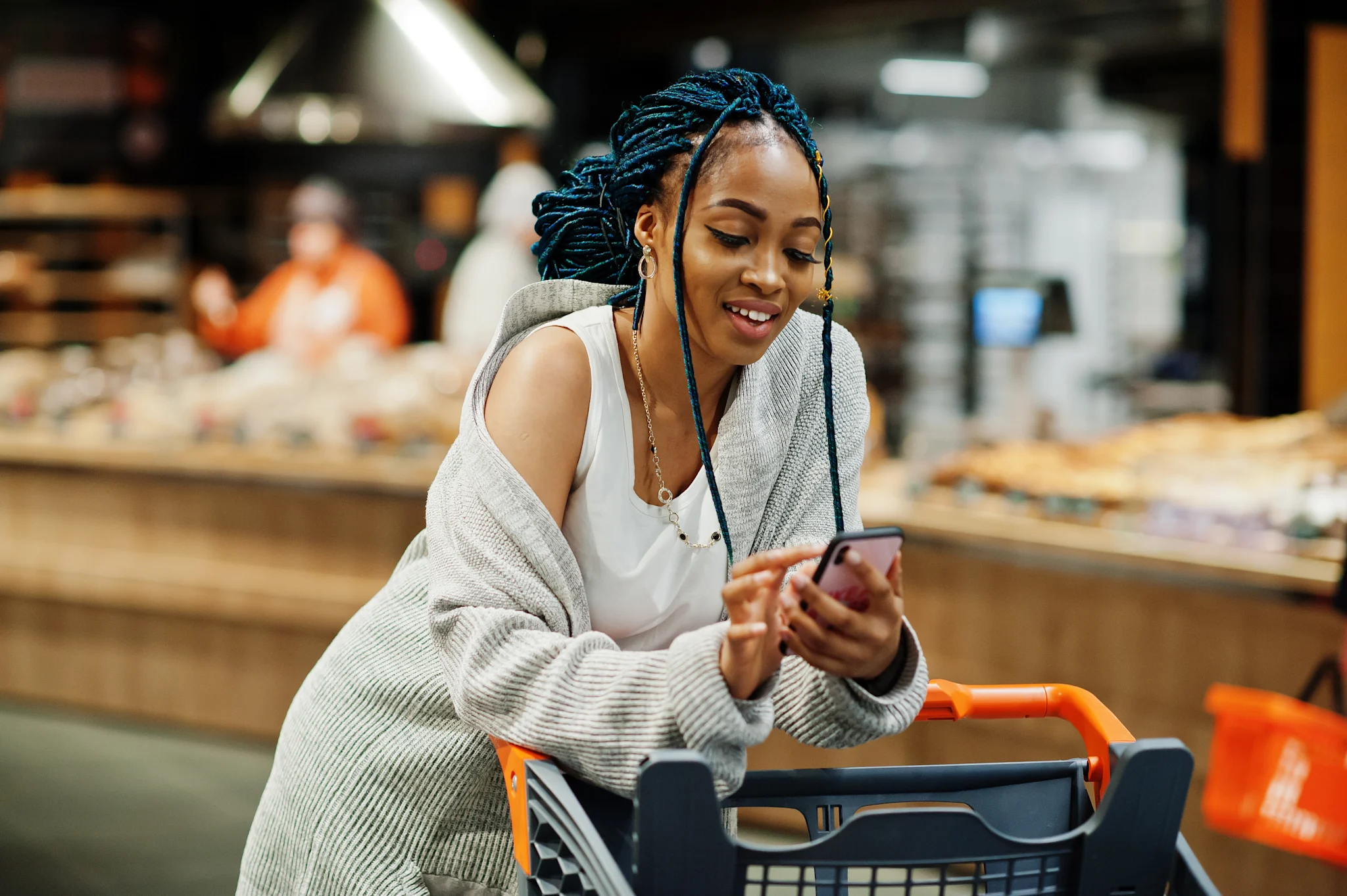 woman leaning over shopping cart scrolling on her phone