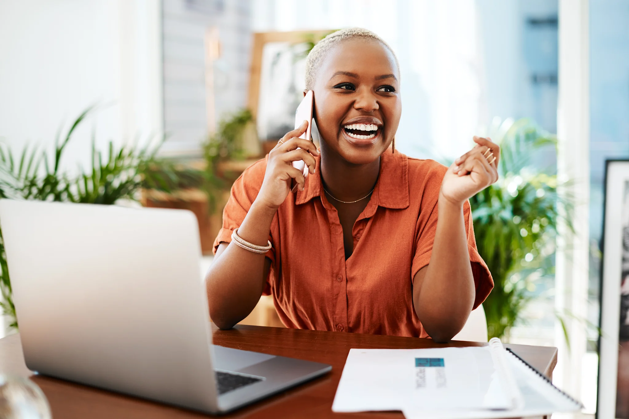 Woman on phone smiling sitting in front of her computer at her desk