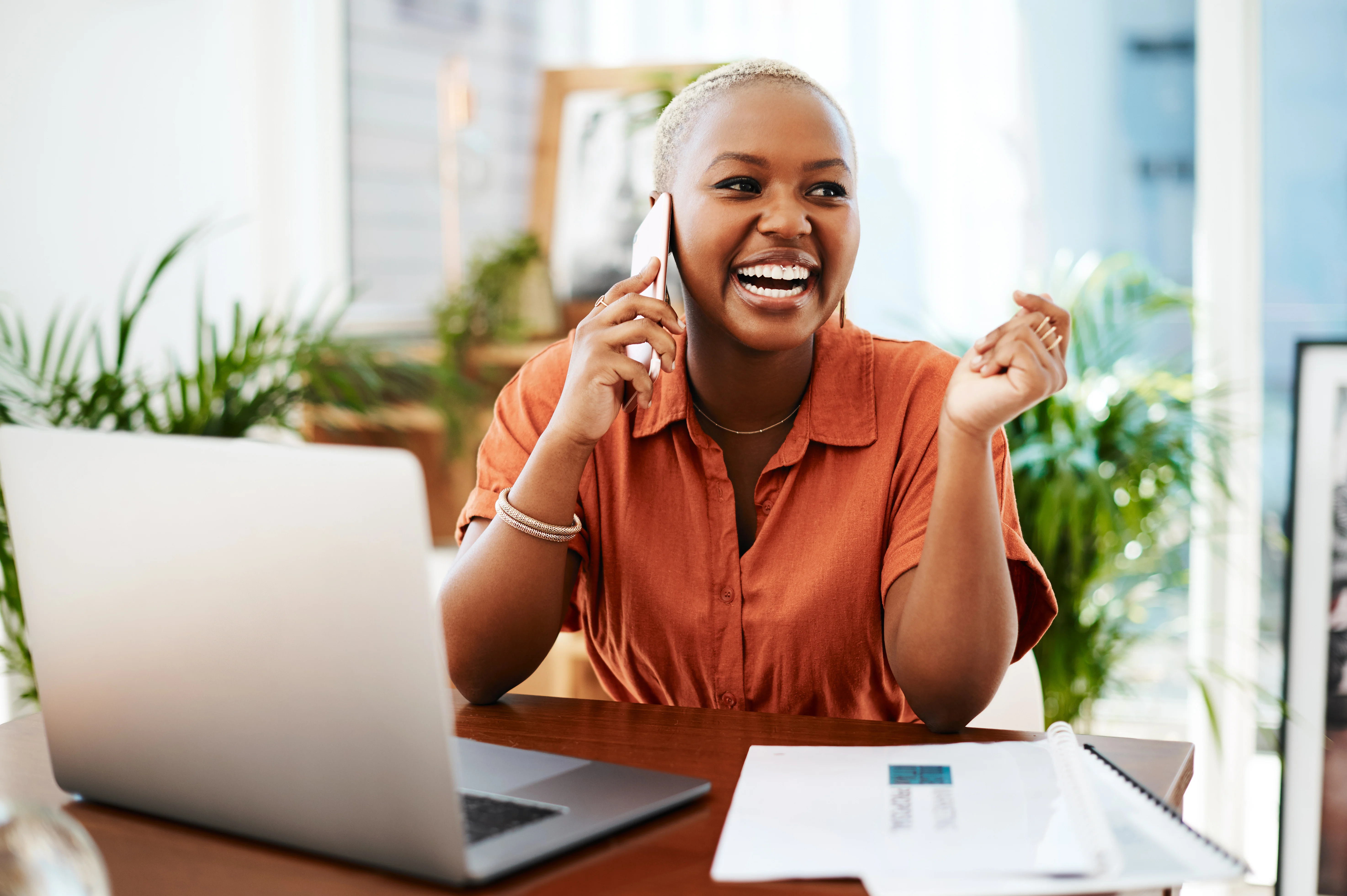 Woman on phone smiling sitting in front of her computer at her desk