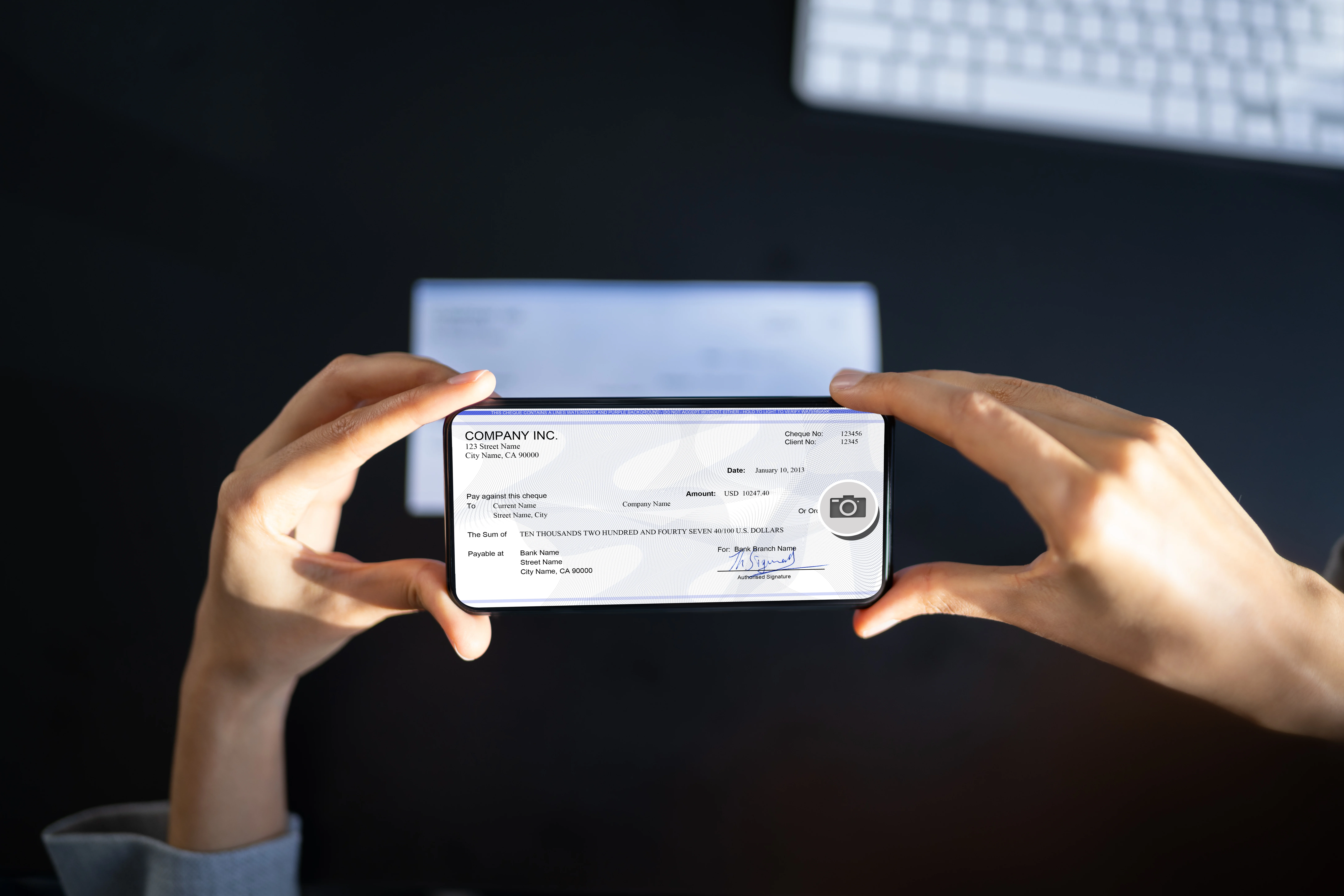 person holding a phone above a check to deposit it