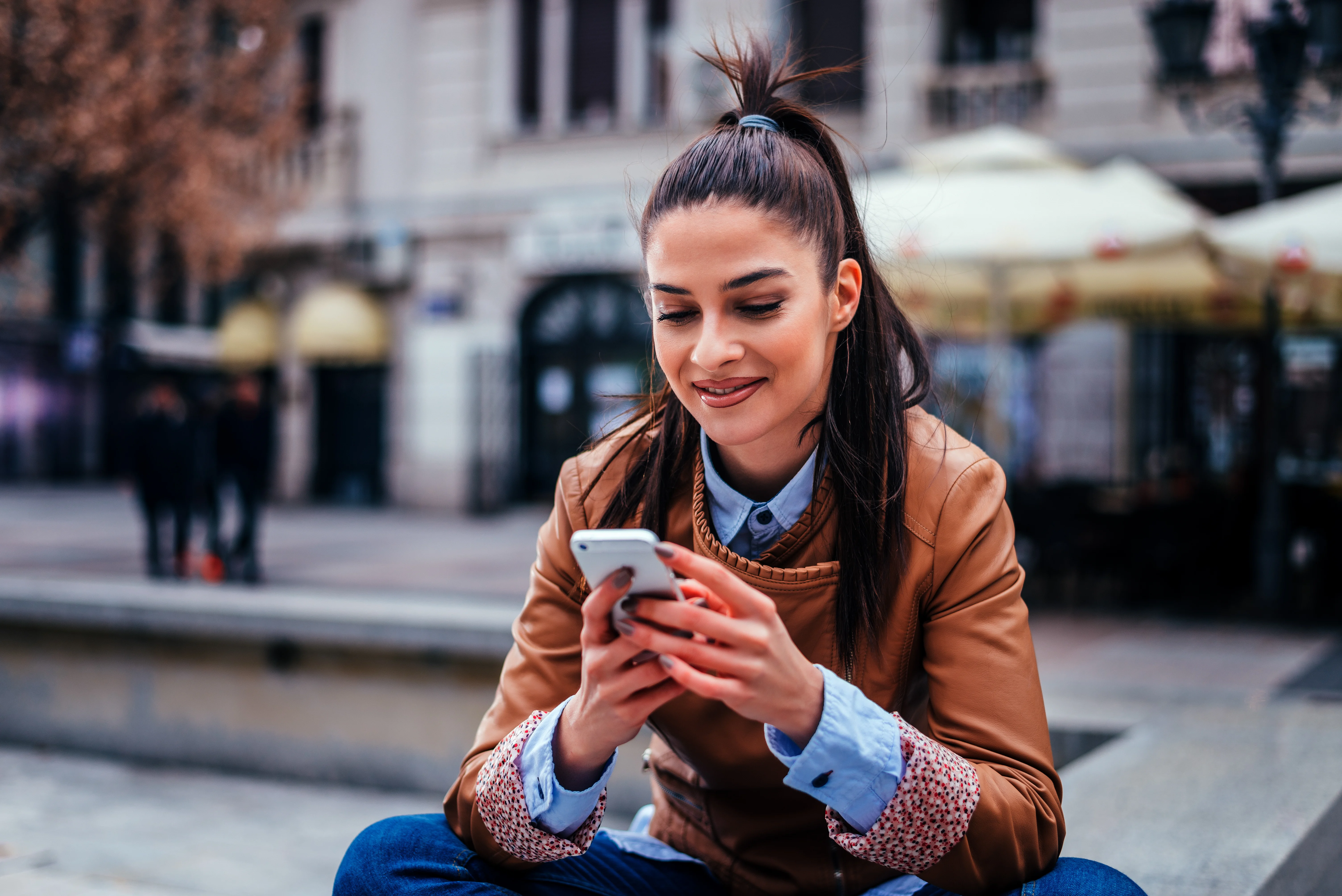 woman with ponytail sitting crosslegged and using her phone