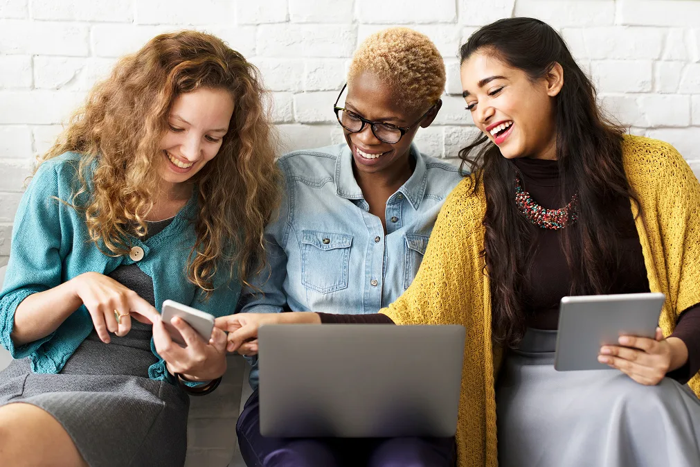 Drei lächelnde Frauen schauen auf ein Smartphone