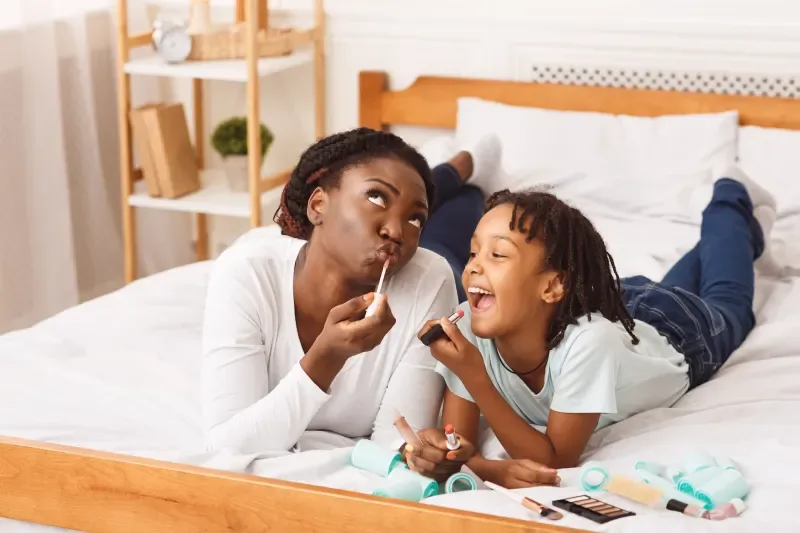 Mutter und Tochter liegen im Bett und schminken Lippen mit Lippenstift