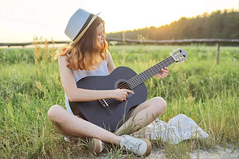 Mädchen mit einer Gitarre sitzt auf dem Gras sitzt