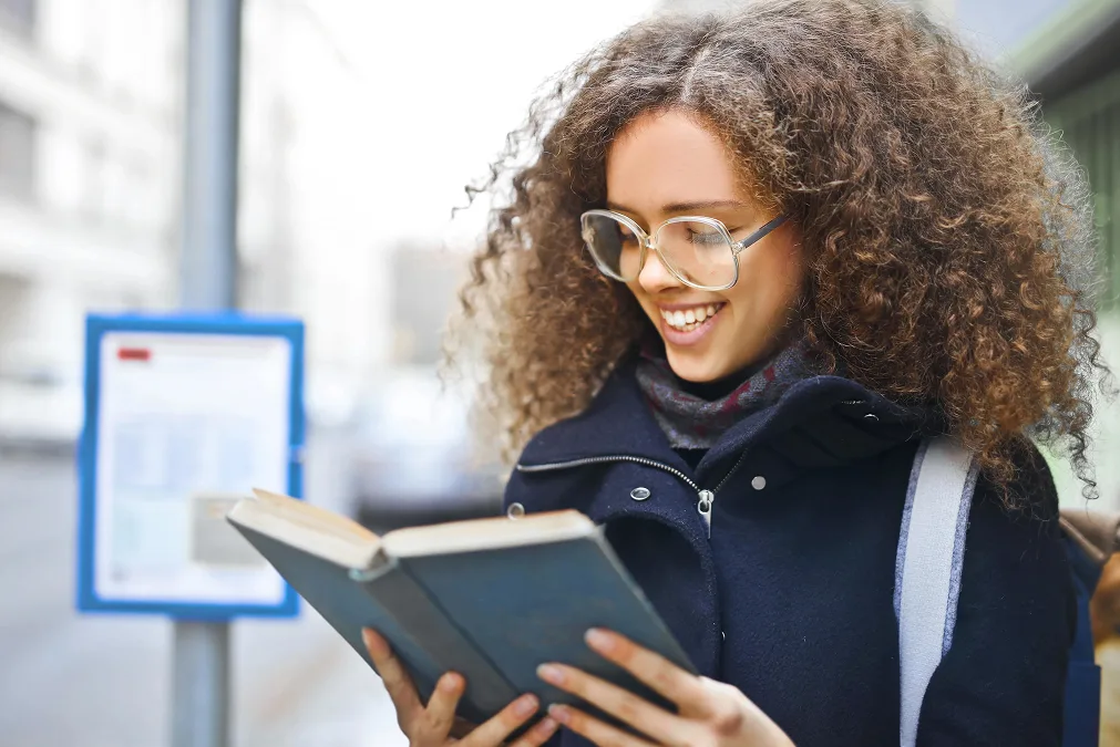 Mädchen steht an der Bushaltestelle und liest ein Buch