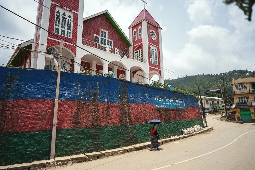 A women walks up a street in Myanmar with a church in the background