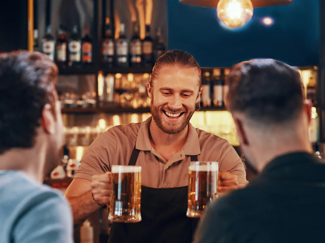 Bartender serving beer to customers at a bar — representing the liquor licensing industry
